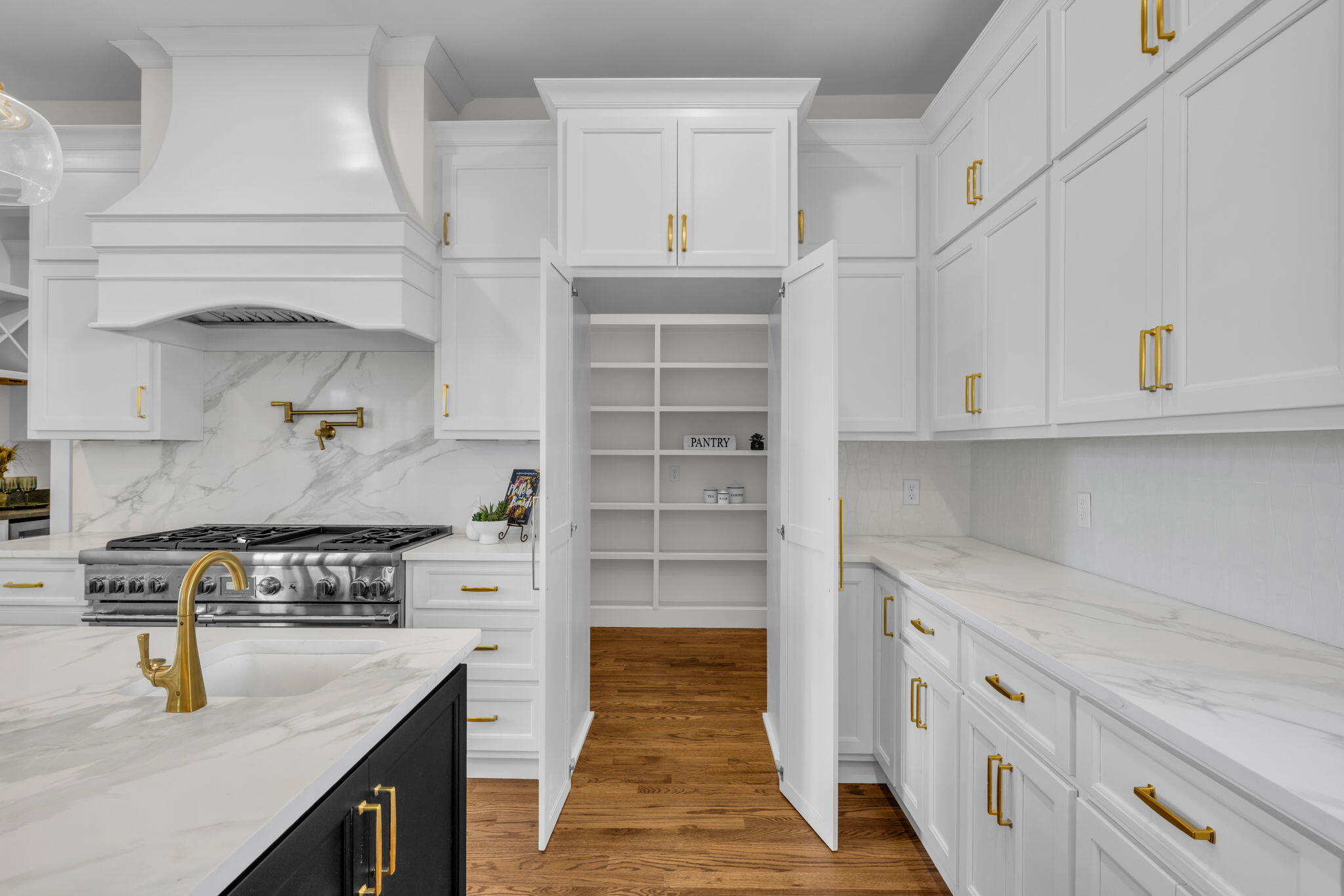 White kitchen with brass hardware and marble-look counters, showing the open pantry’s built-in shelves.