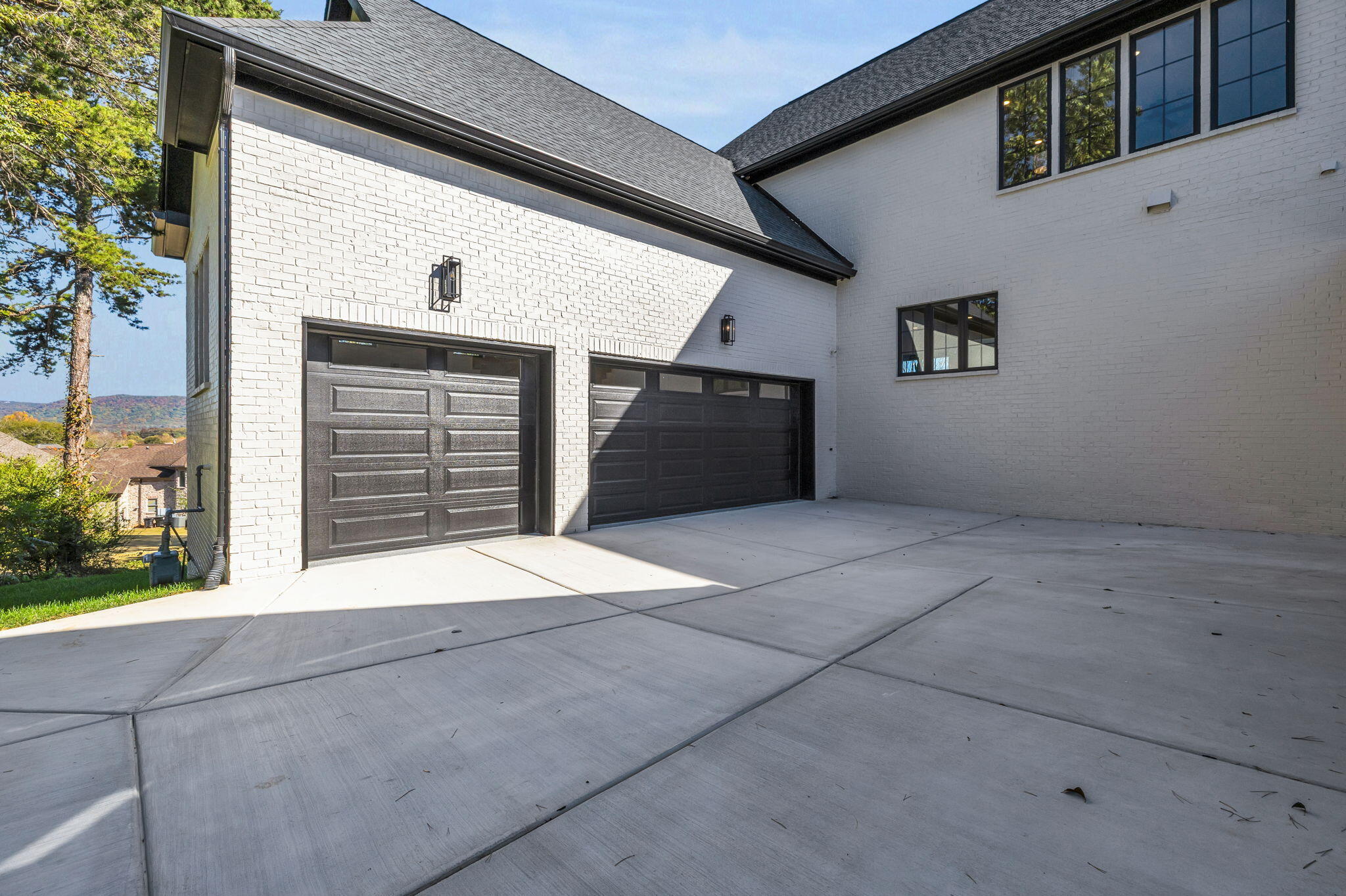 White brick home with two dark garage doors and a broad concrete driveway.