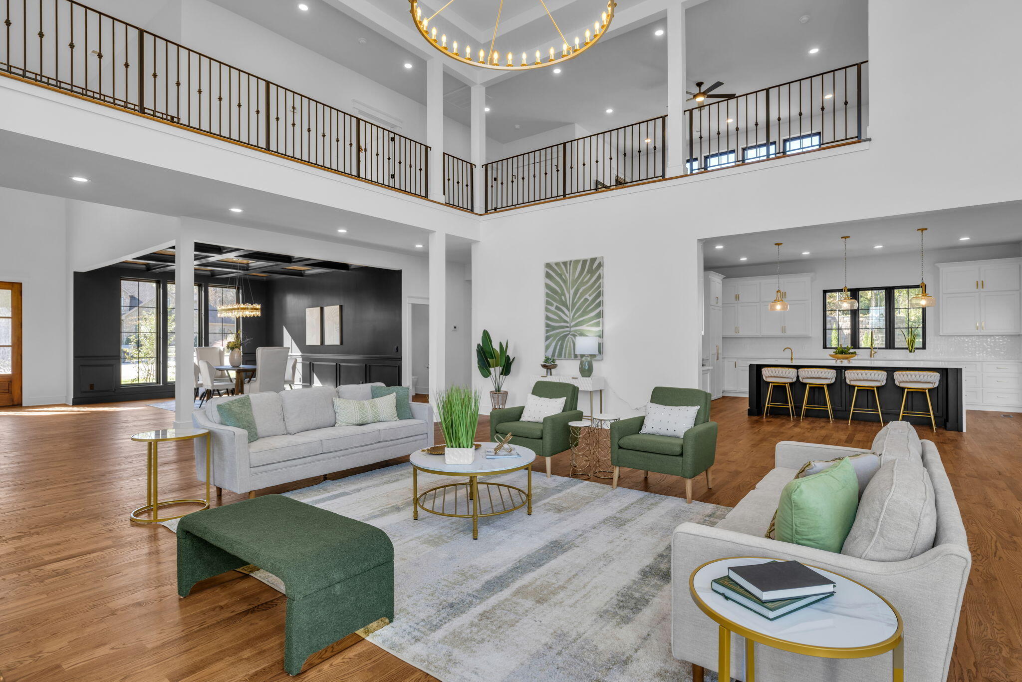 Open-plan living room with a double-height ceiling, upstairs overlook, green chairs, and adjoining white kitchen.