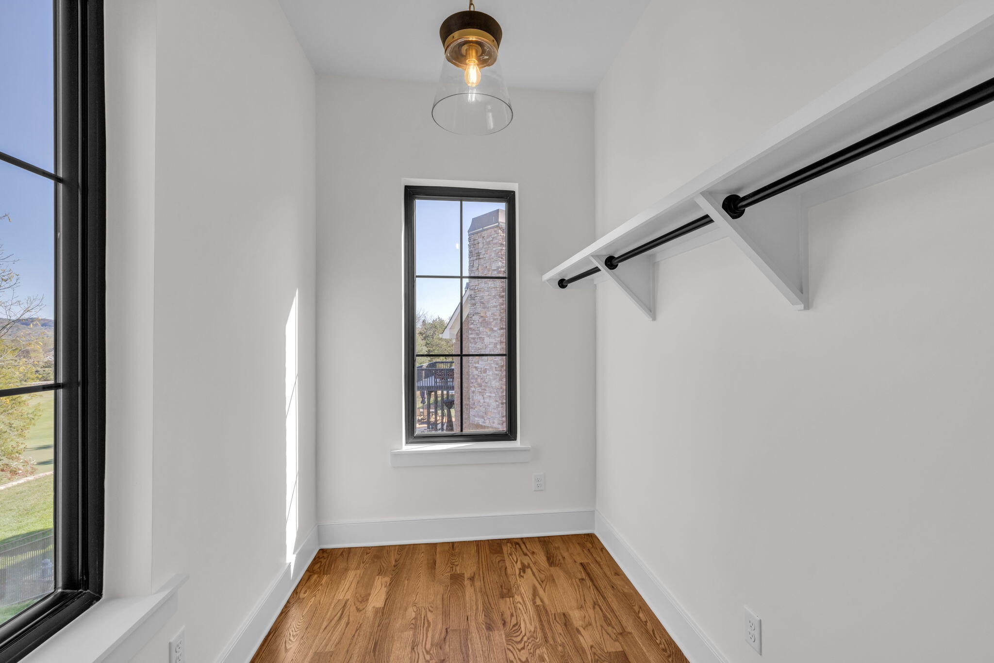 Walk-in closet with built-in black hanging rods, hardwood floors, and tall black-framed windows.