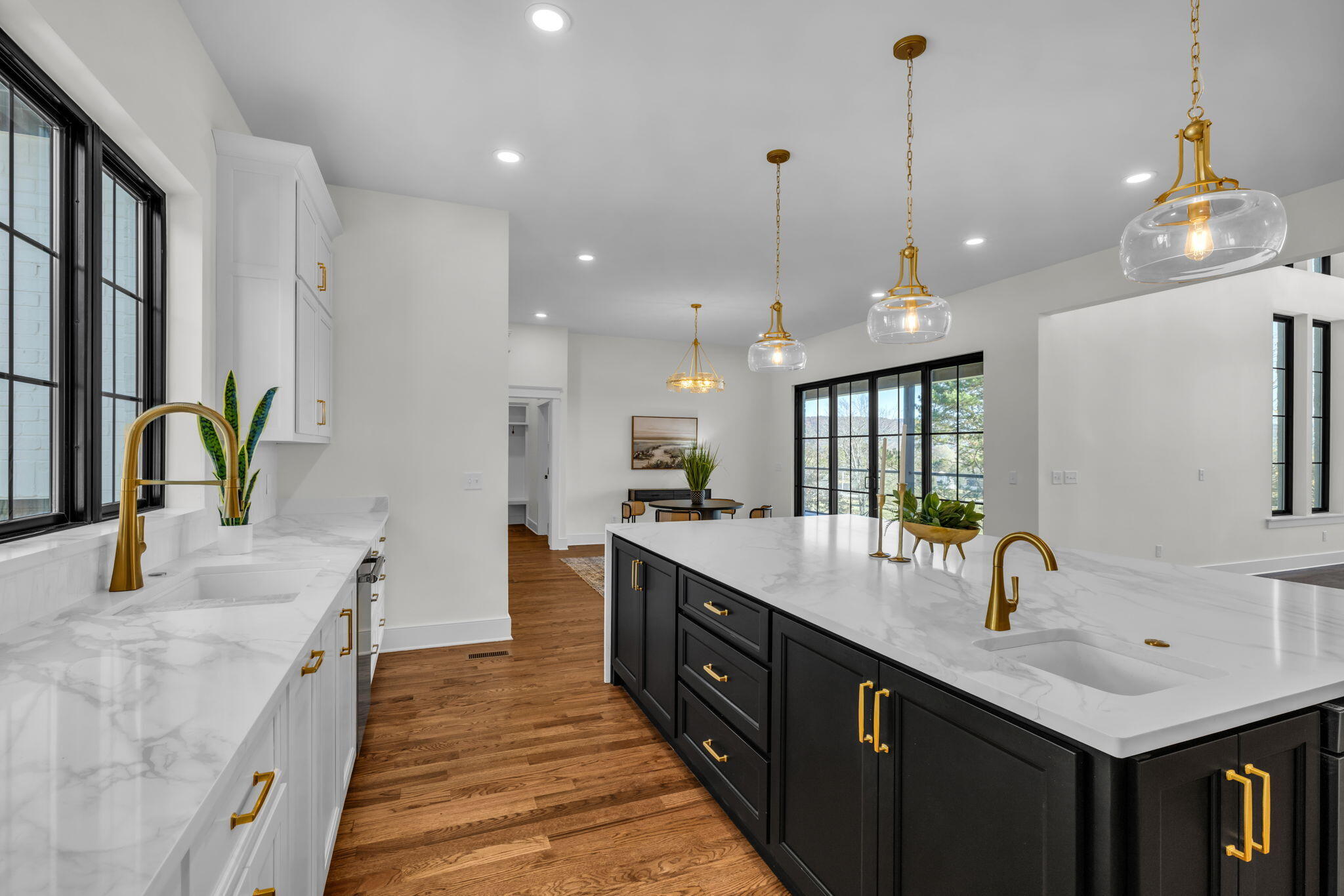 Kitchen with a large black island, marble-look counters, gold fixtures, and hardwood floors.