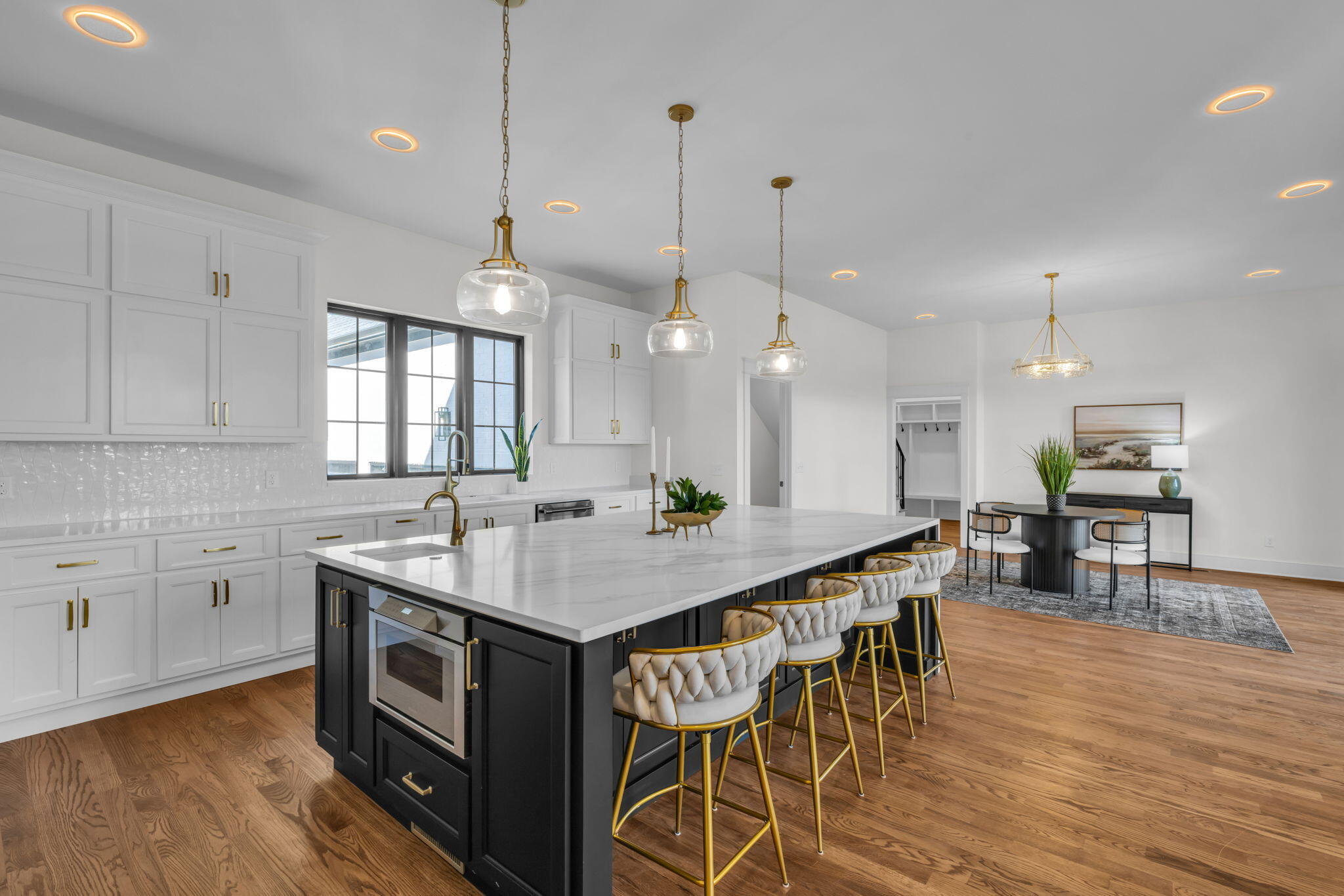 Open kitchen with a large black island, white stone counters, gold fixtures, and tufted bar stools.
