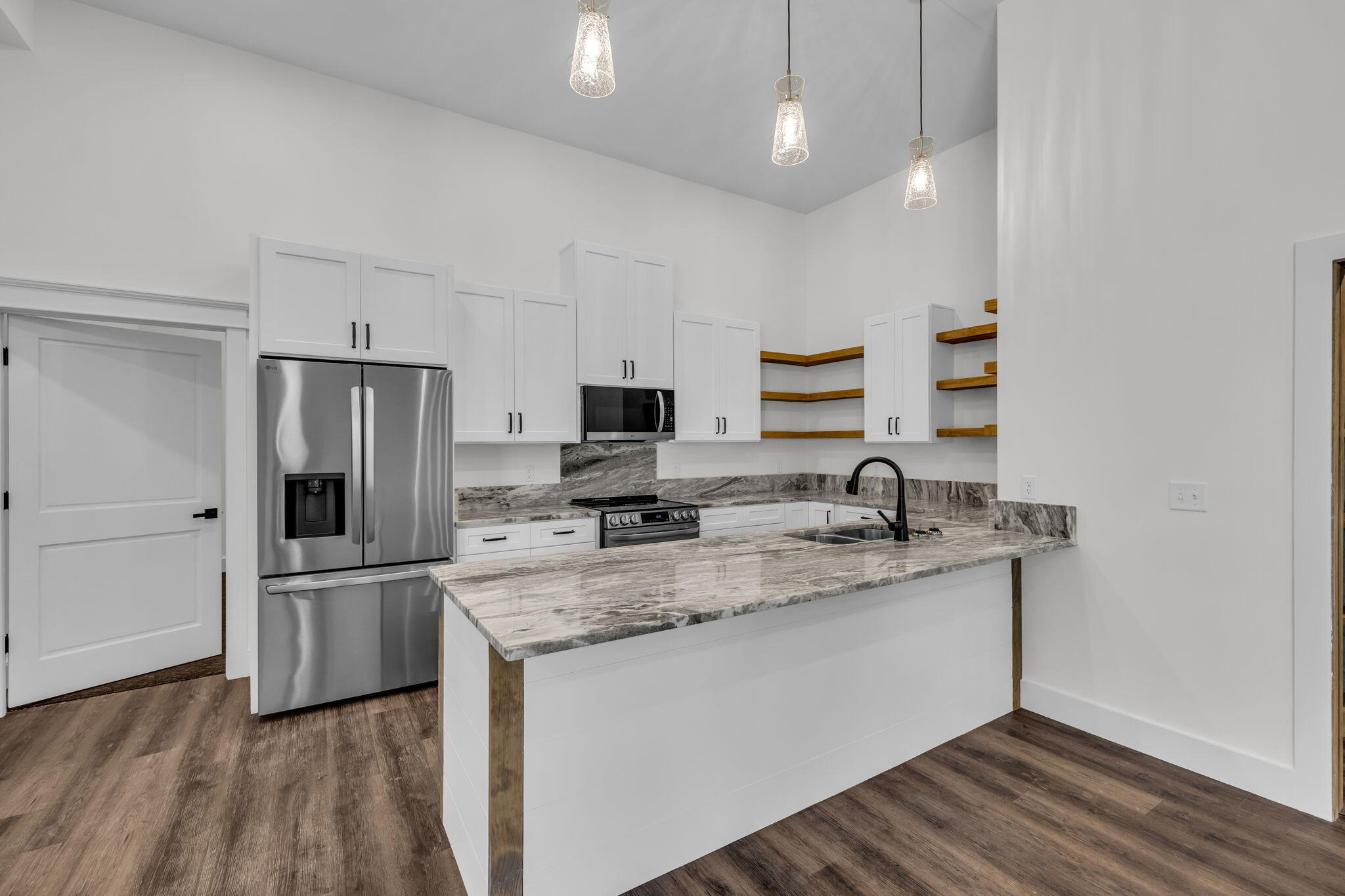 Modern kitchen with a large stone island, white cabinets, stainless appliances, and open wooden shelves.
