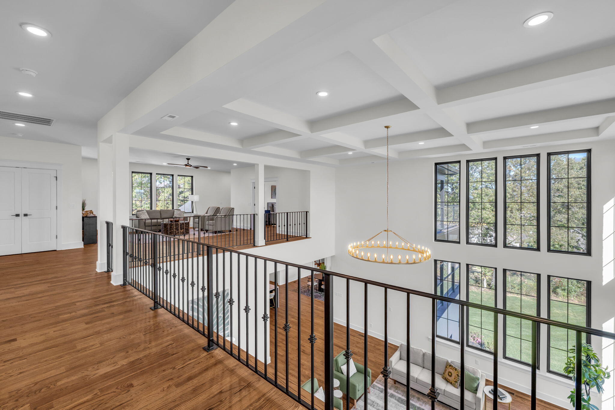Upper landing overlooks a furnished two-story living room with tall windows and a circular chandelier.