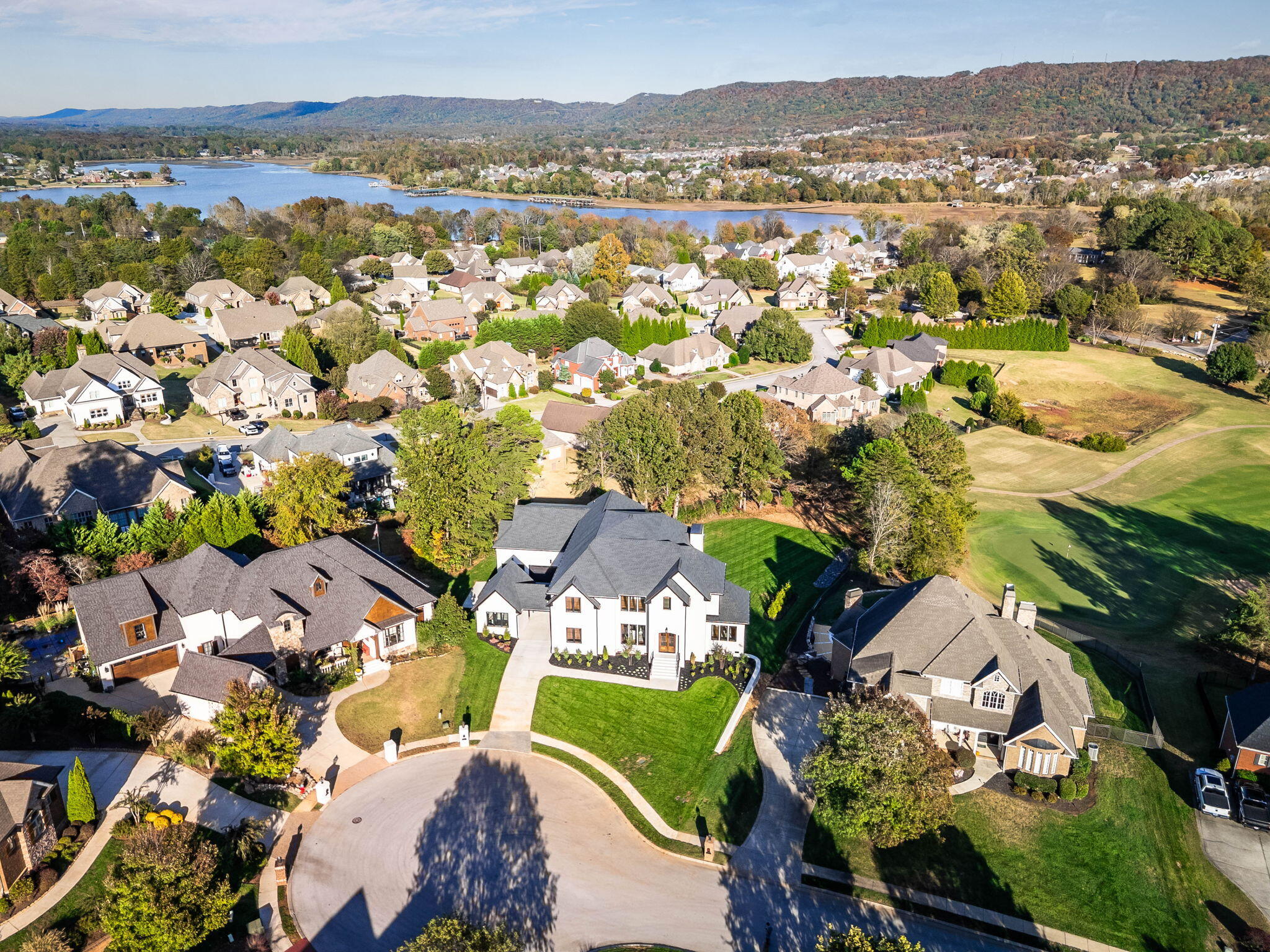 Aerial view of a white home on a cul-de-sac, with a lake and wooded hills beyond the neighborhood.