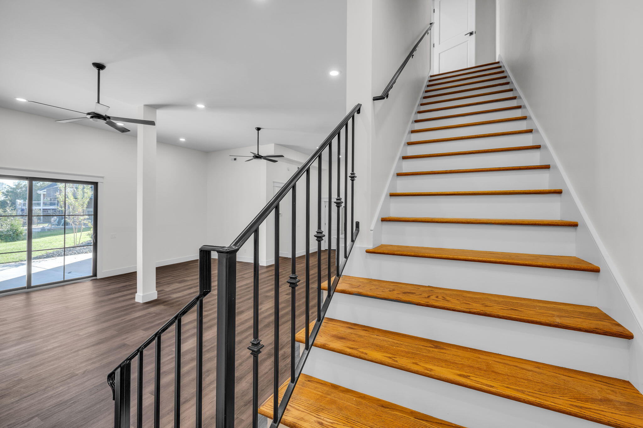 Open-plan interior with a wood-tread staircase, black railing, and sliding glass doors to a patio.