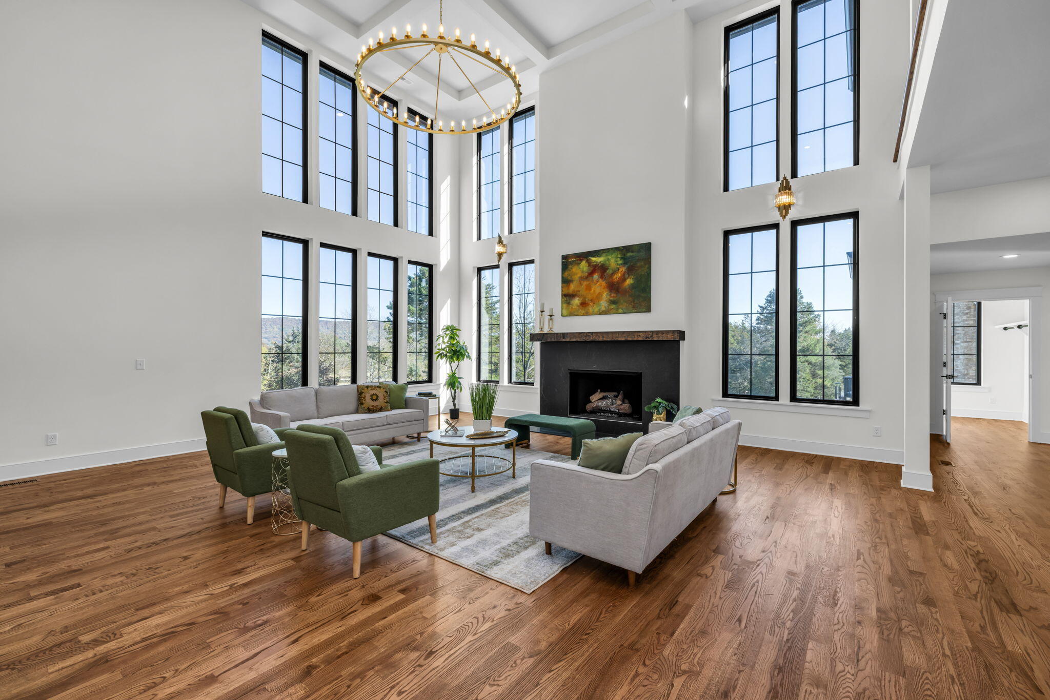 Double-height living room with a fireplace, tall windows, brass chandelier, and hardwood floors.
