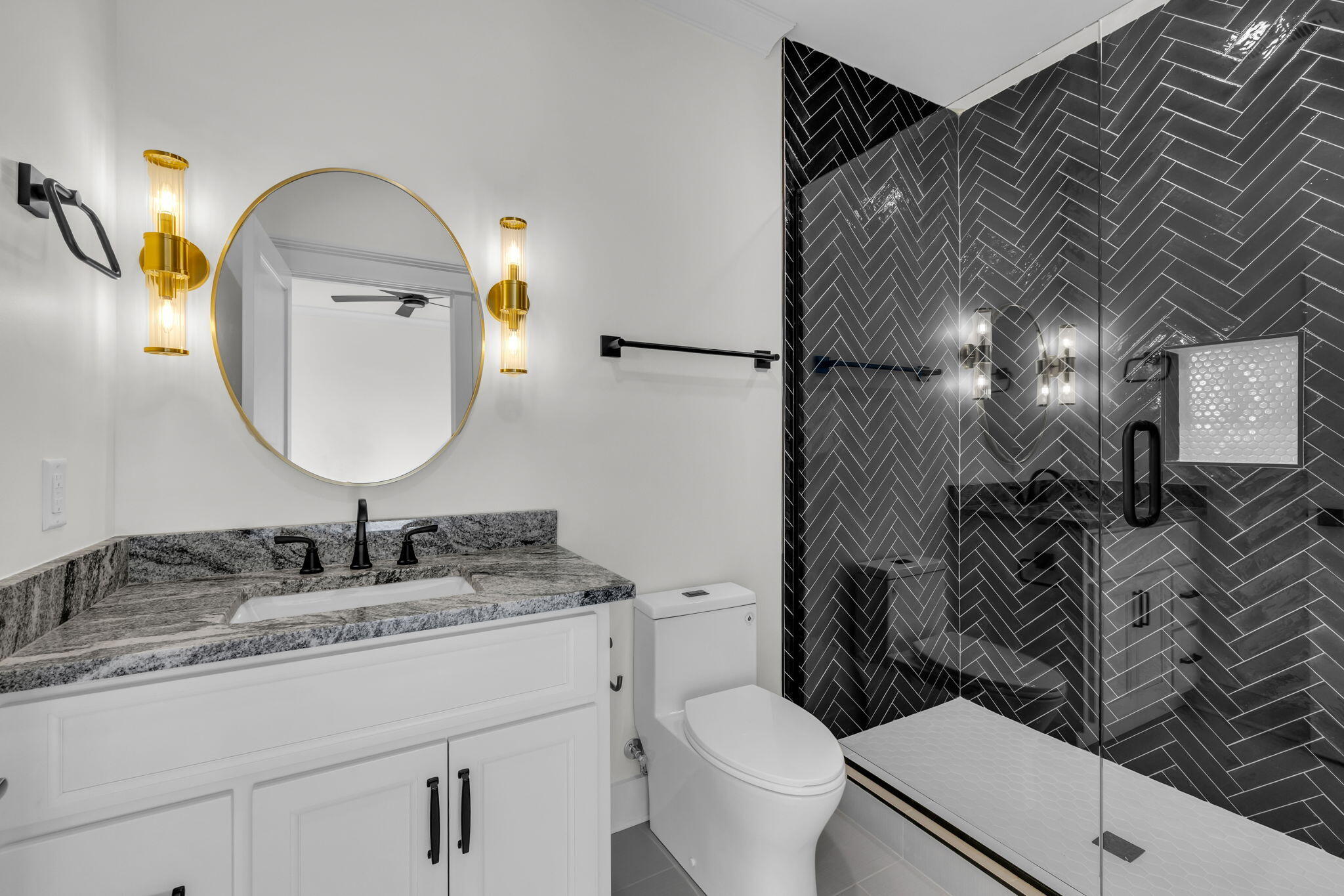 Bathroom with a granite vanity and glass shower lined in dark herringbone tile.