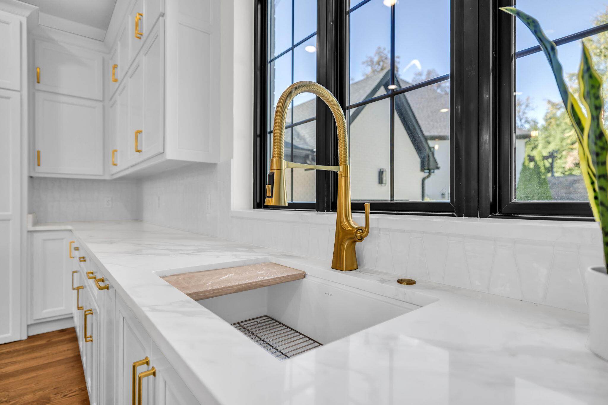 White kitchen sink with a gold faucet beneath black-framed windows.
