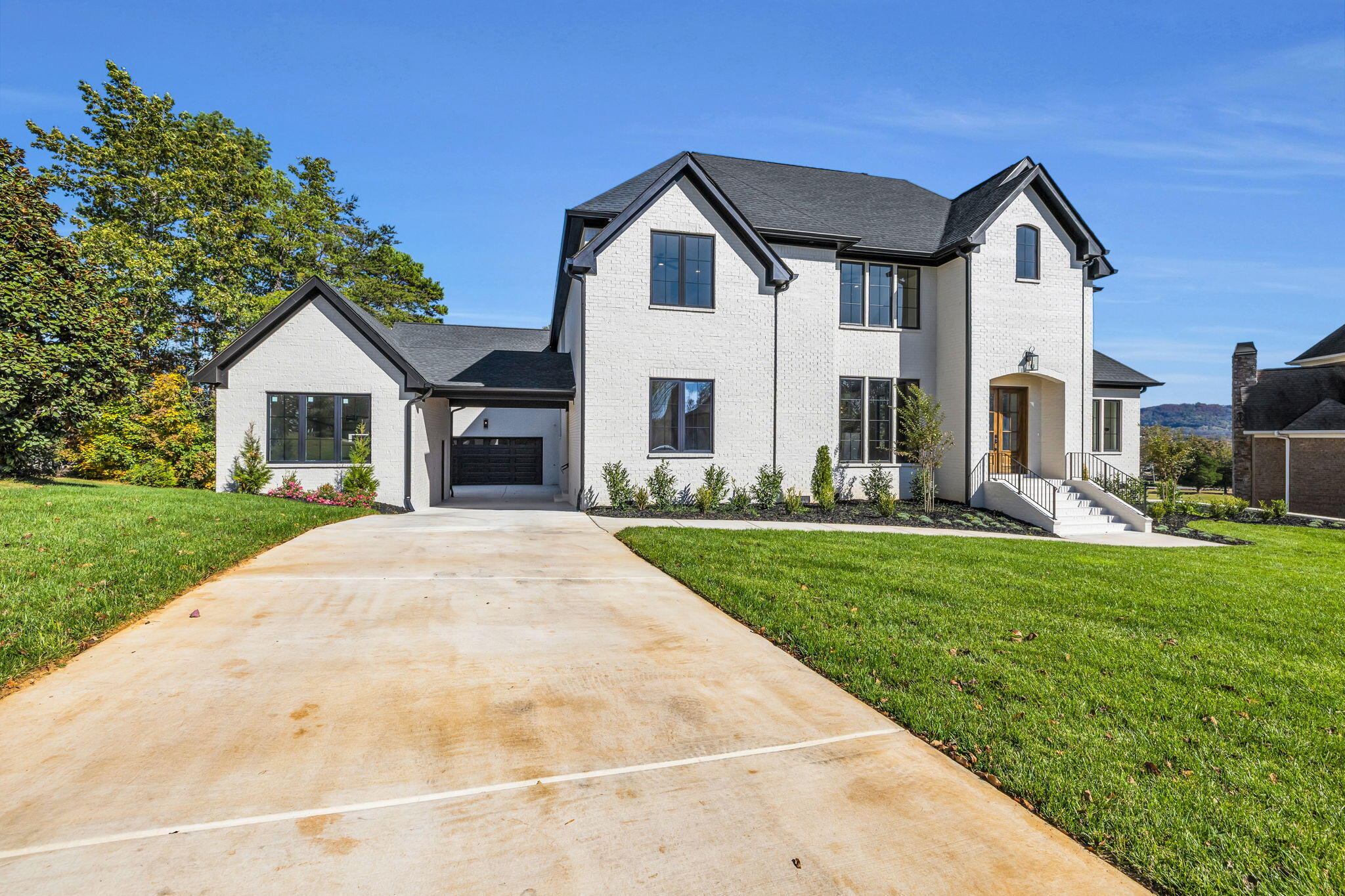 Two-story white brick home with dark gabled roofs, attached garage, and broad concrete driveway.