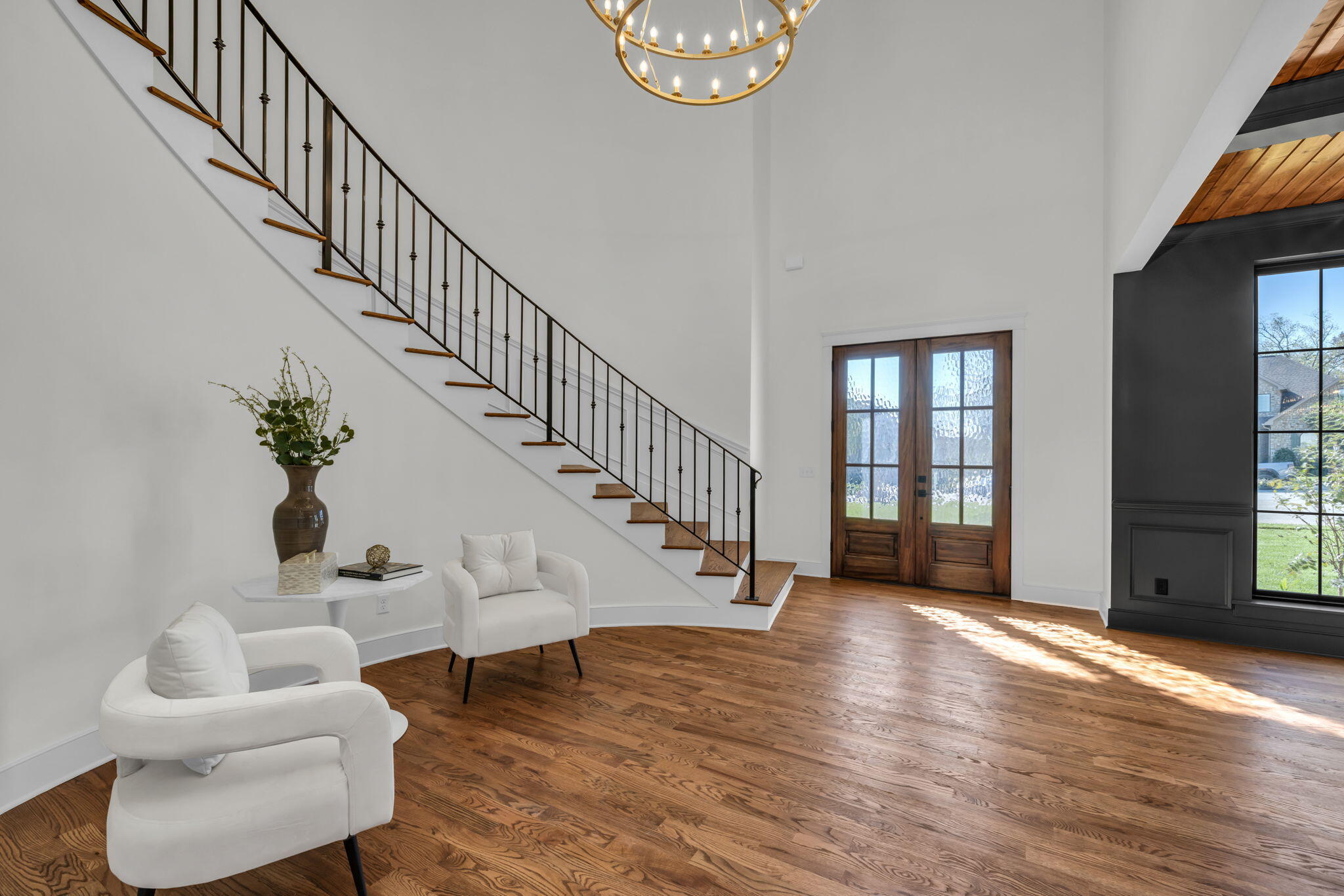 Entry foyer with a sweeping staircase, wood front doors, hardwood floors, and white armchairs.
