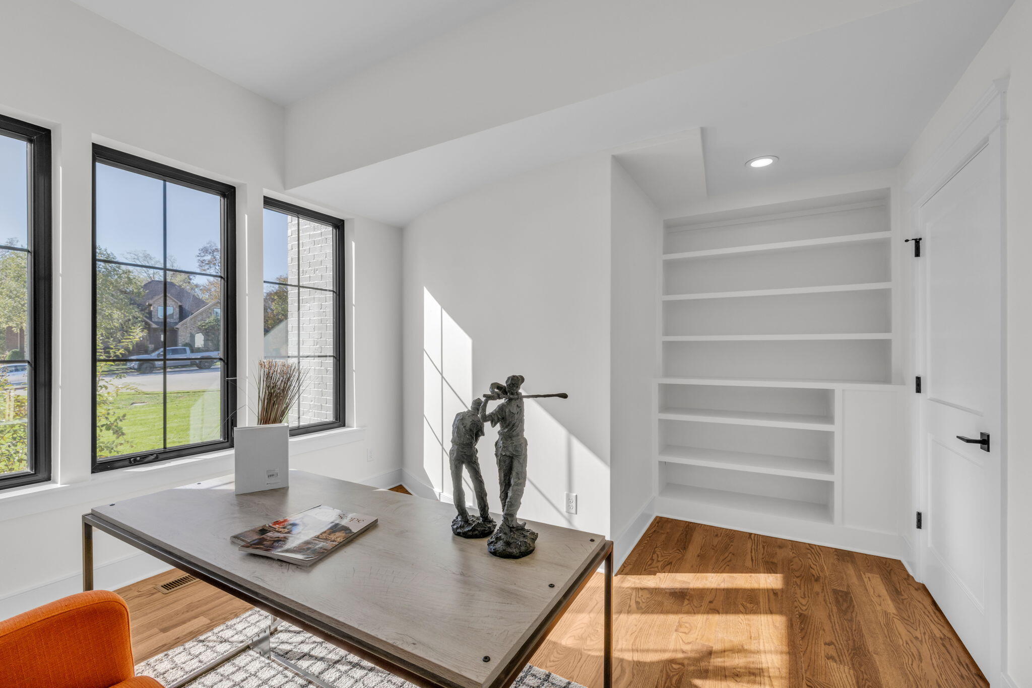 Bright home office with built-in shelving, black-framed windows, and a desk displaying two sculptures.