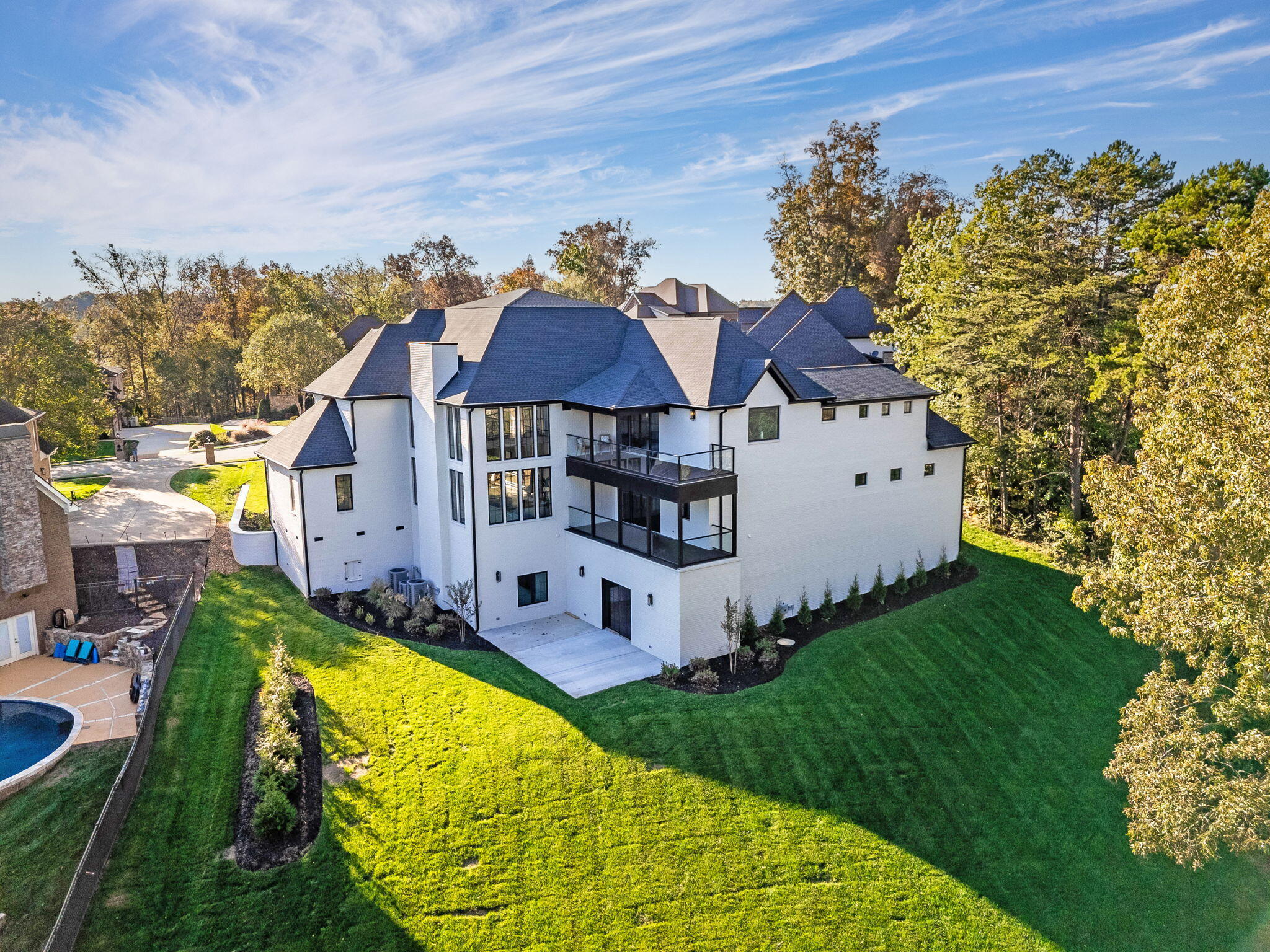 Aerial view of a white multi-story home with glass balconies, a broad lawn, and autumn trees.