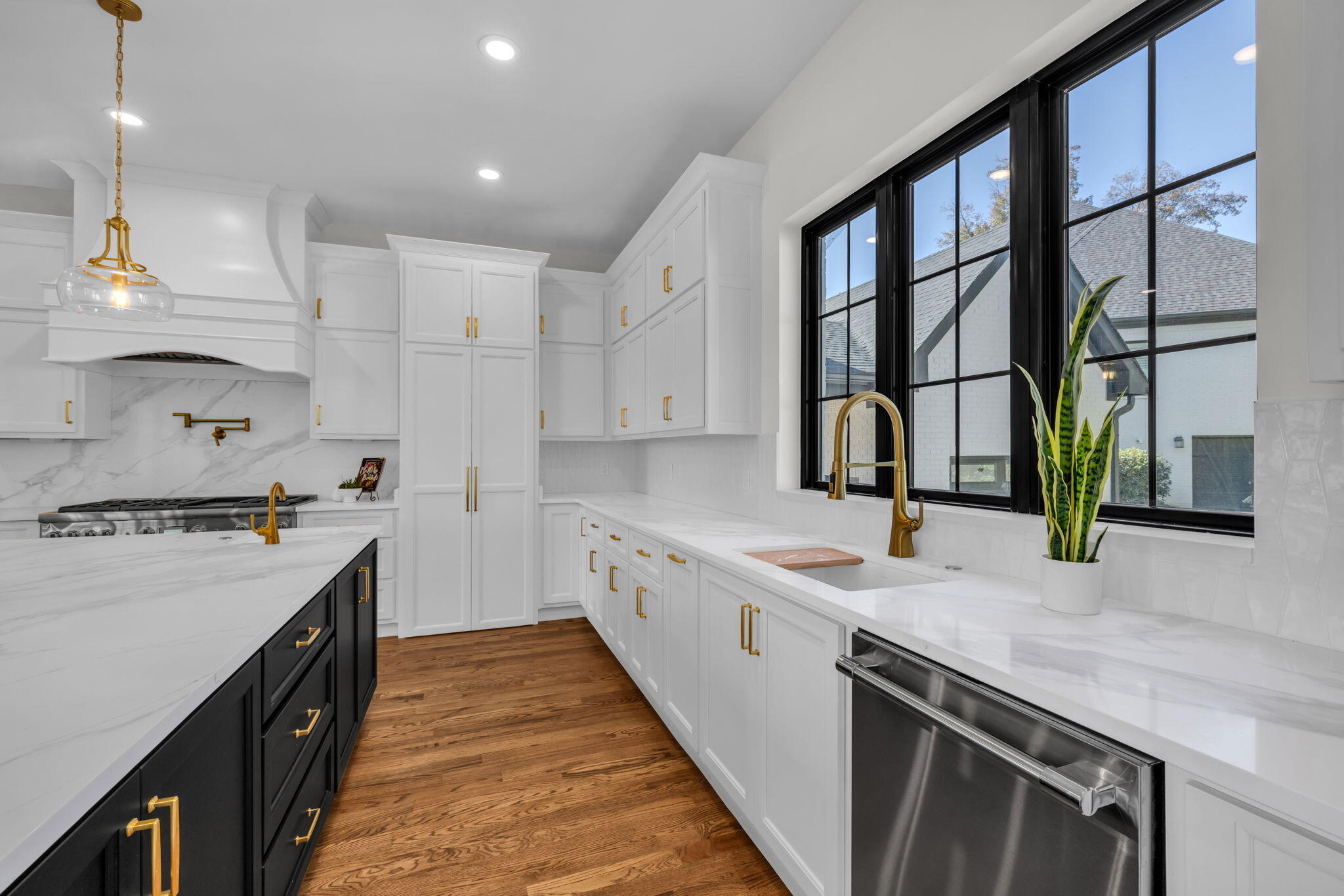Bright white kitchen with a black island, gold fixtures, and large windows above the sink.