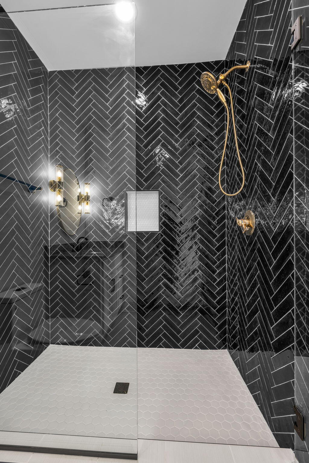 Walk-in shower with black herringbone tile, white hexagon floor, and brass fixtures.