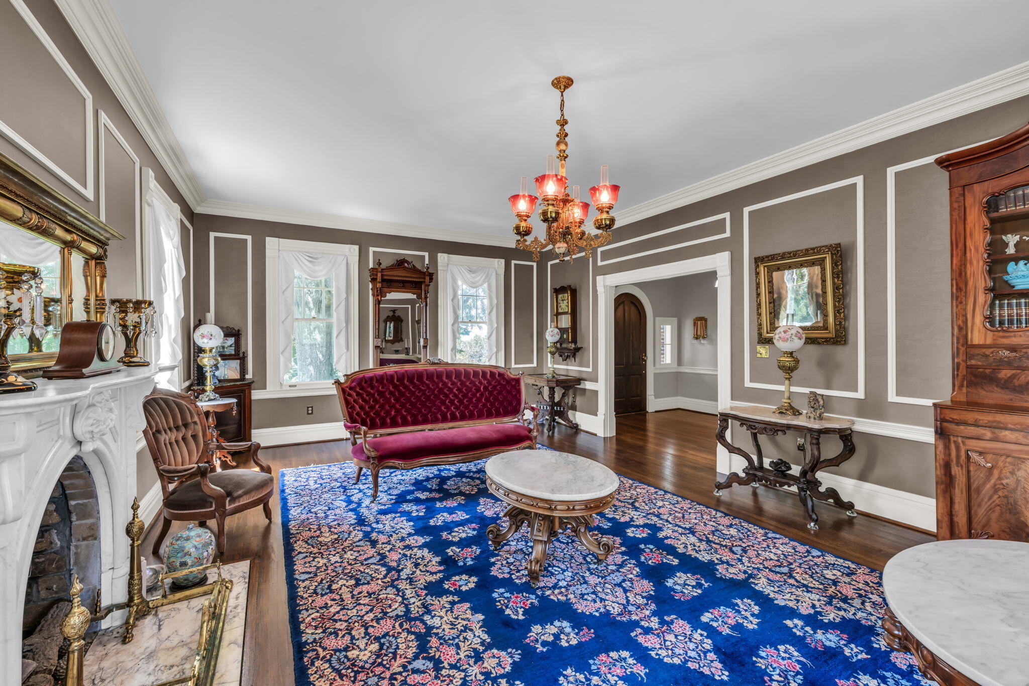 Living room with a marble fireplace, burgundy settee, antique furnishings, and a blue floral rug.