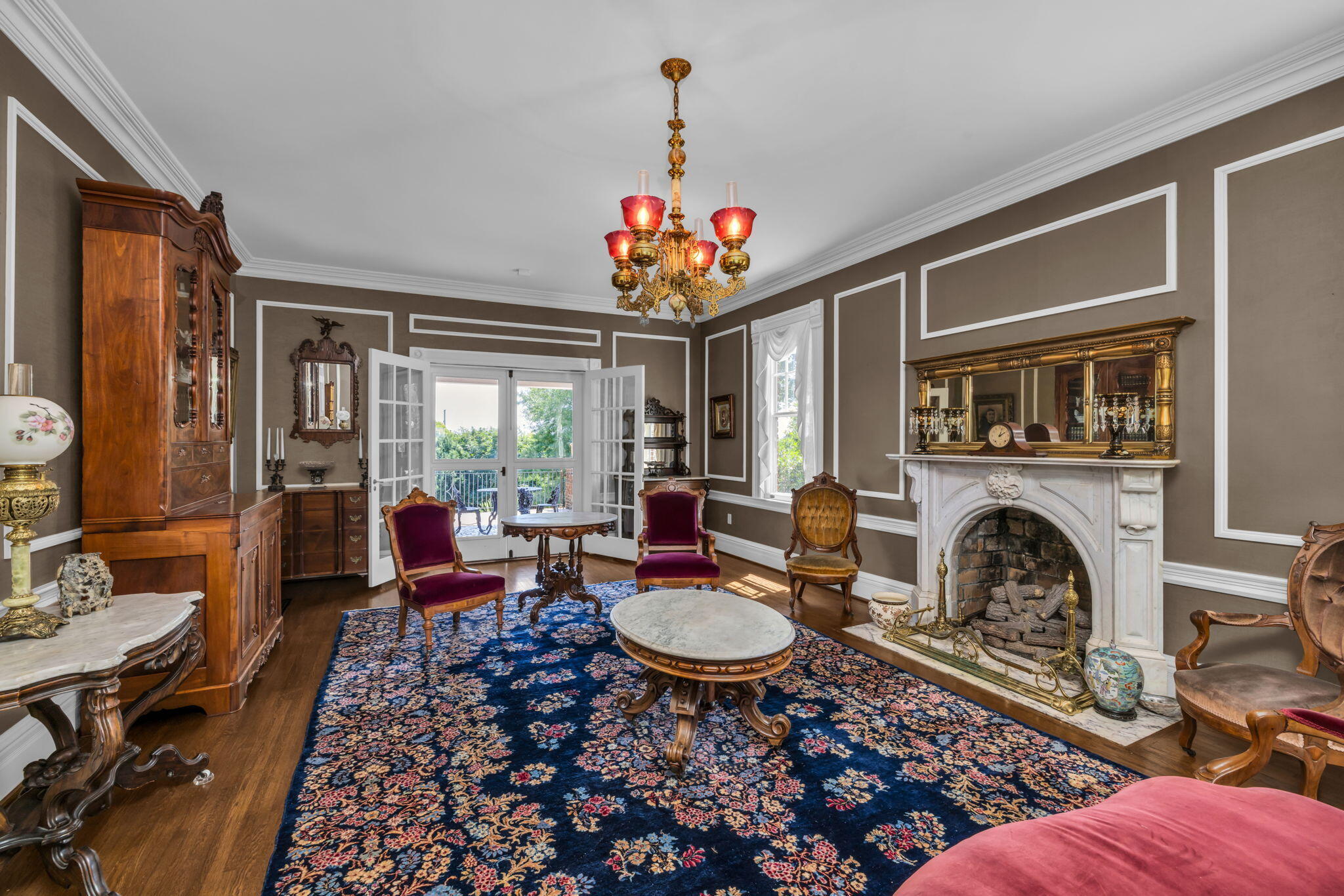Formal living room with antique furnishings, a white fireplace, and open French doors to a balcony.