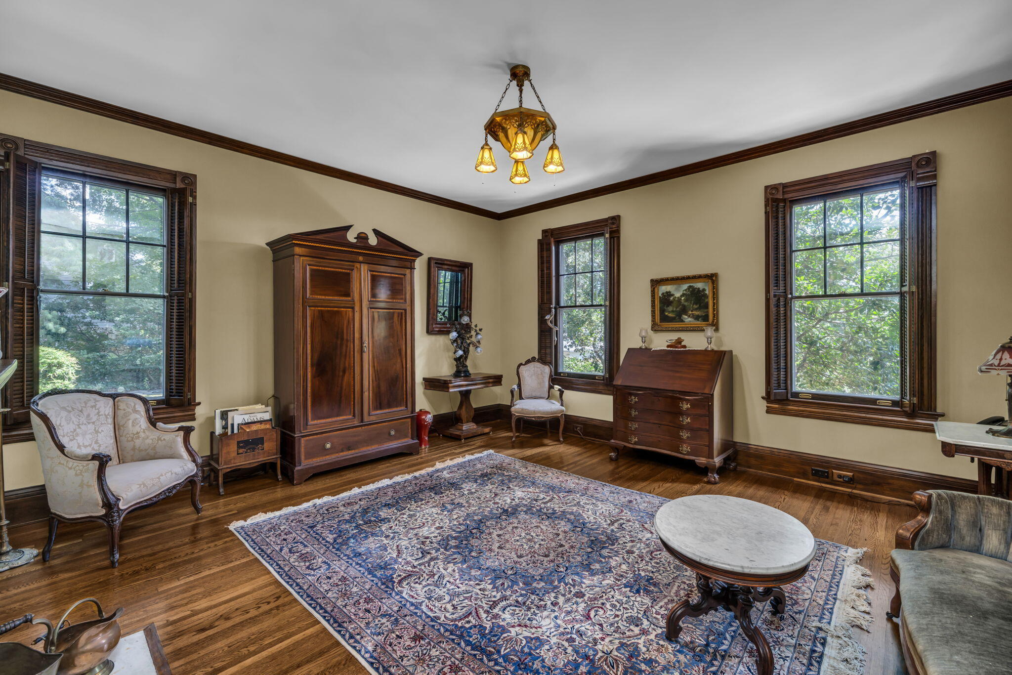 Formal sitting room with antique furniture, tall wood-trimmed windows, and a large patterned rug.