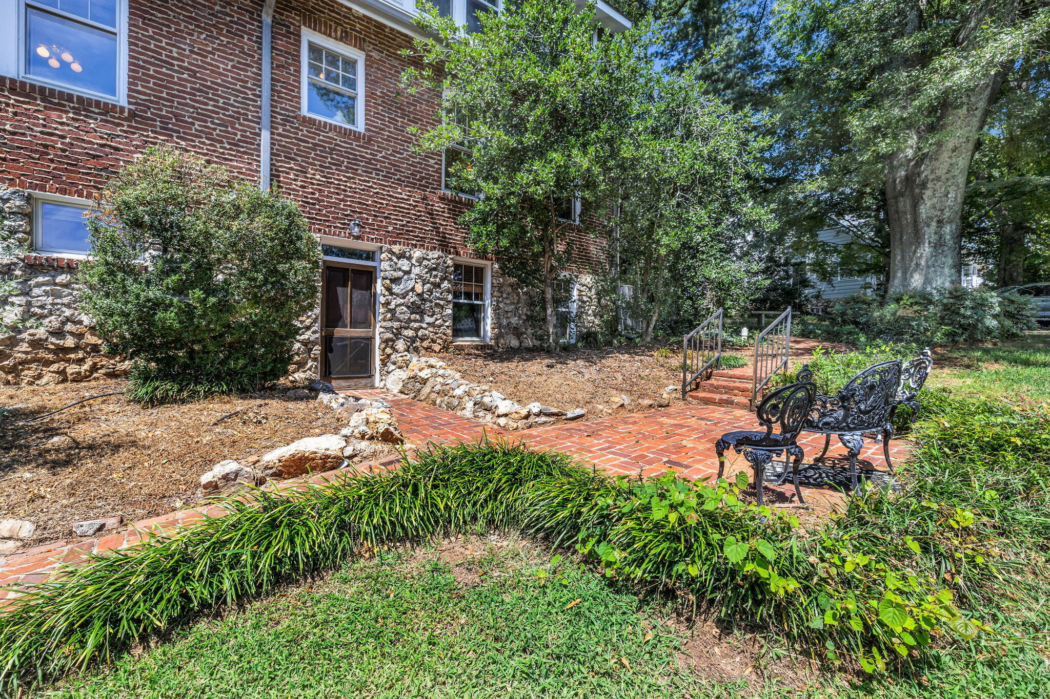 Brick and stone home beside a landscaped brick patio with ornate metal benches.