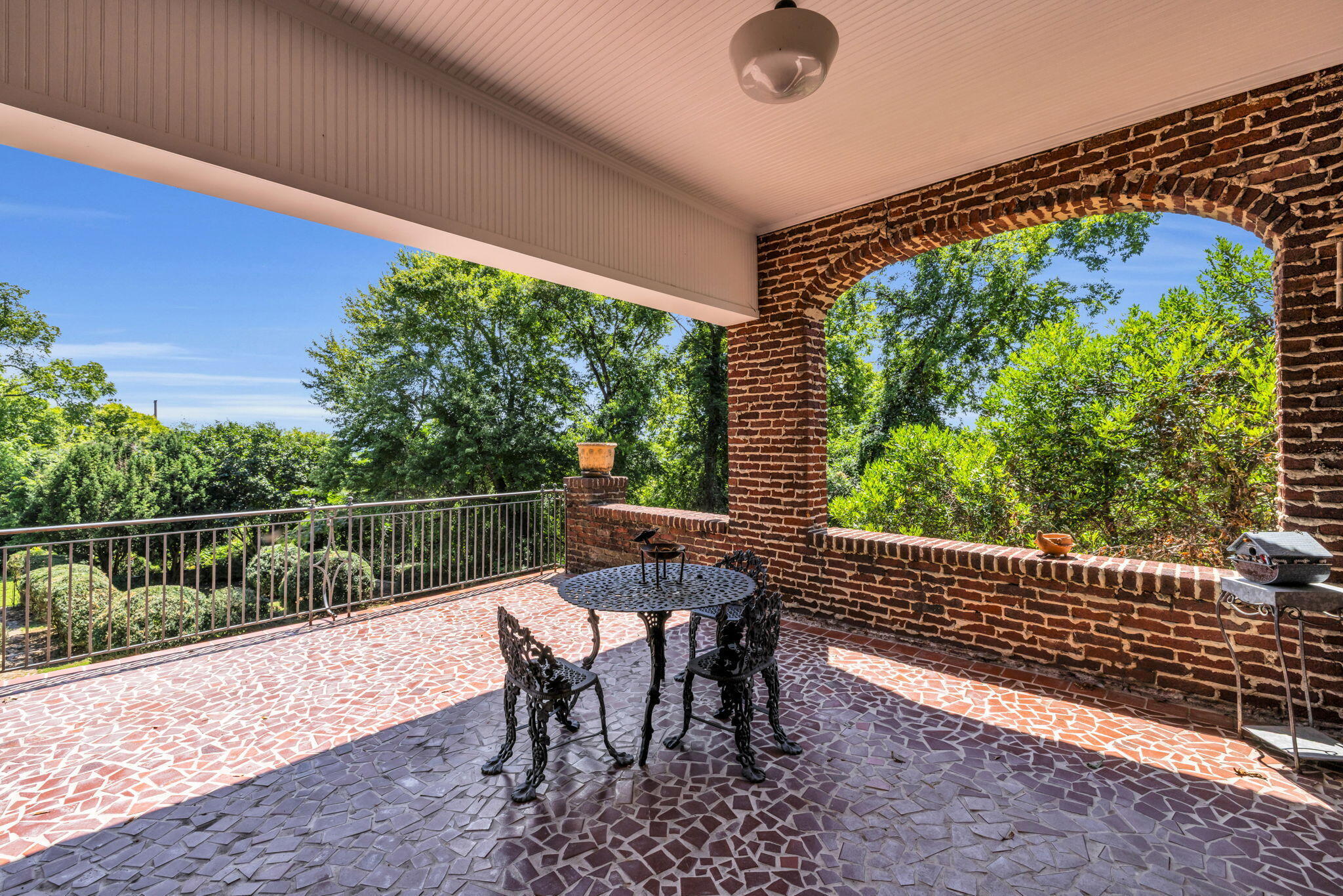 Covered brick patio with stone flooring, black metal dining set, and leafy green views.