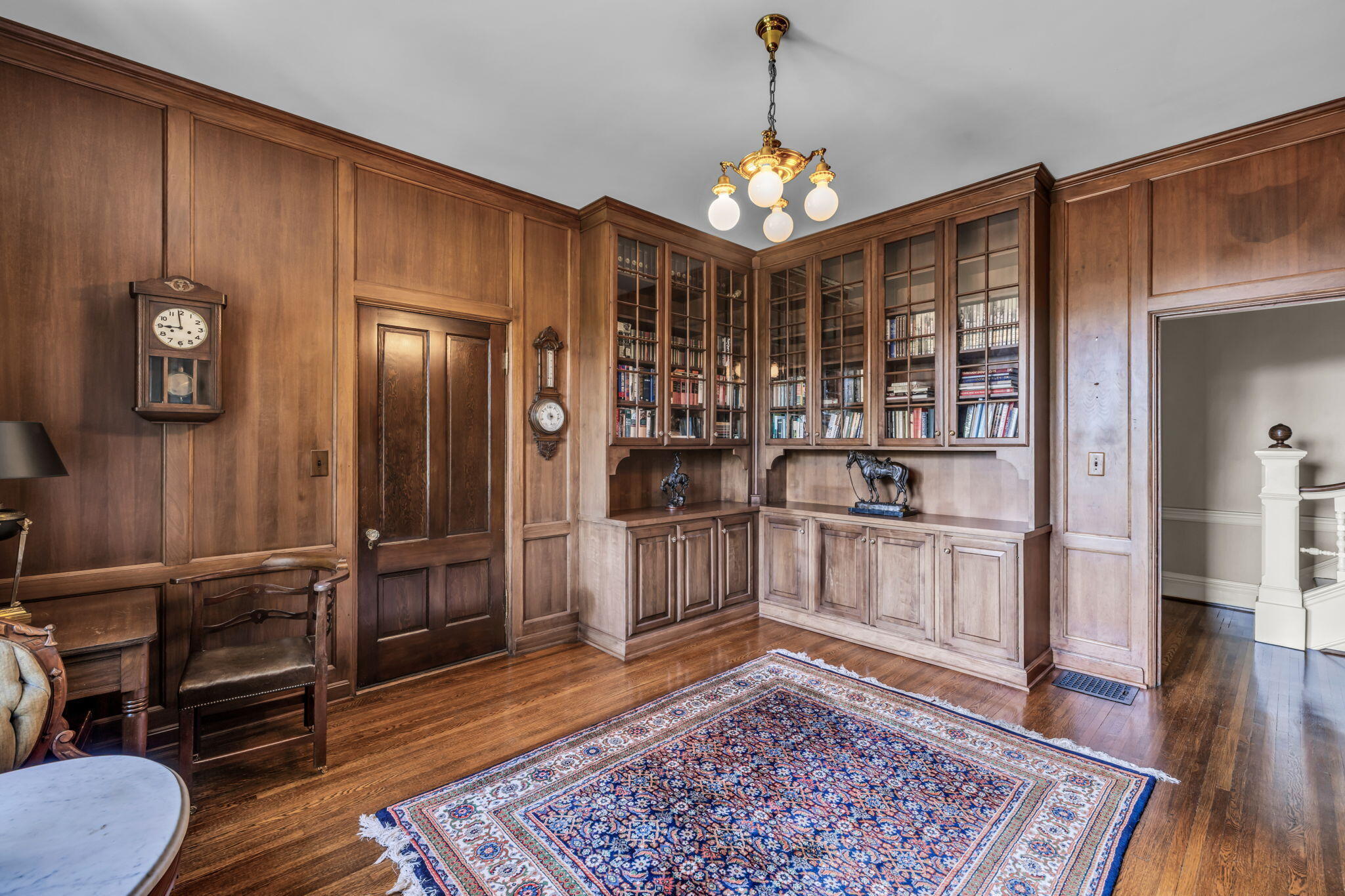 Wood-paneled study with built-in bookcases, hardwood floors, and a patterned rug.