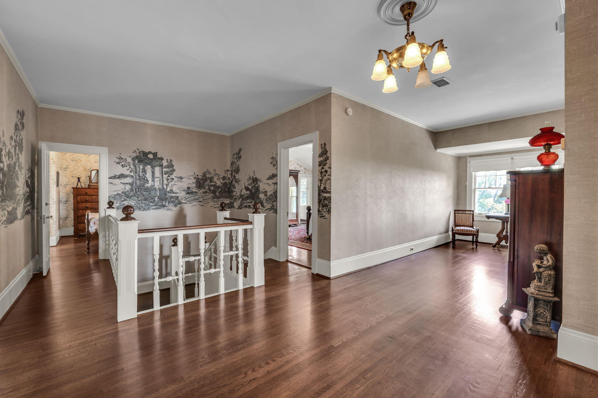 Upstairs landing with hardwood floors, white stair railing, and scenic mural wallpaper.