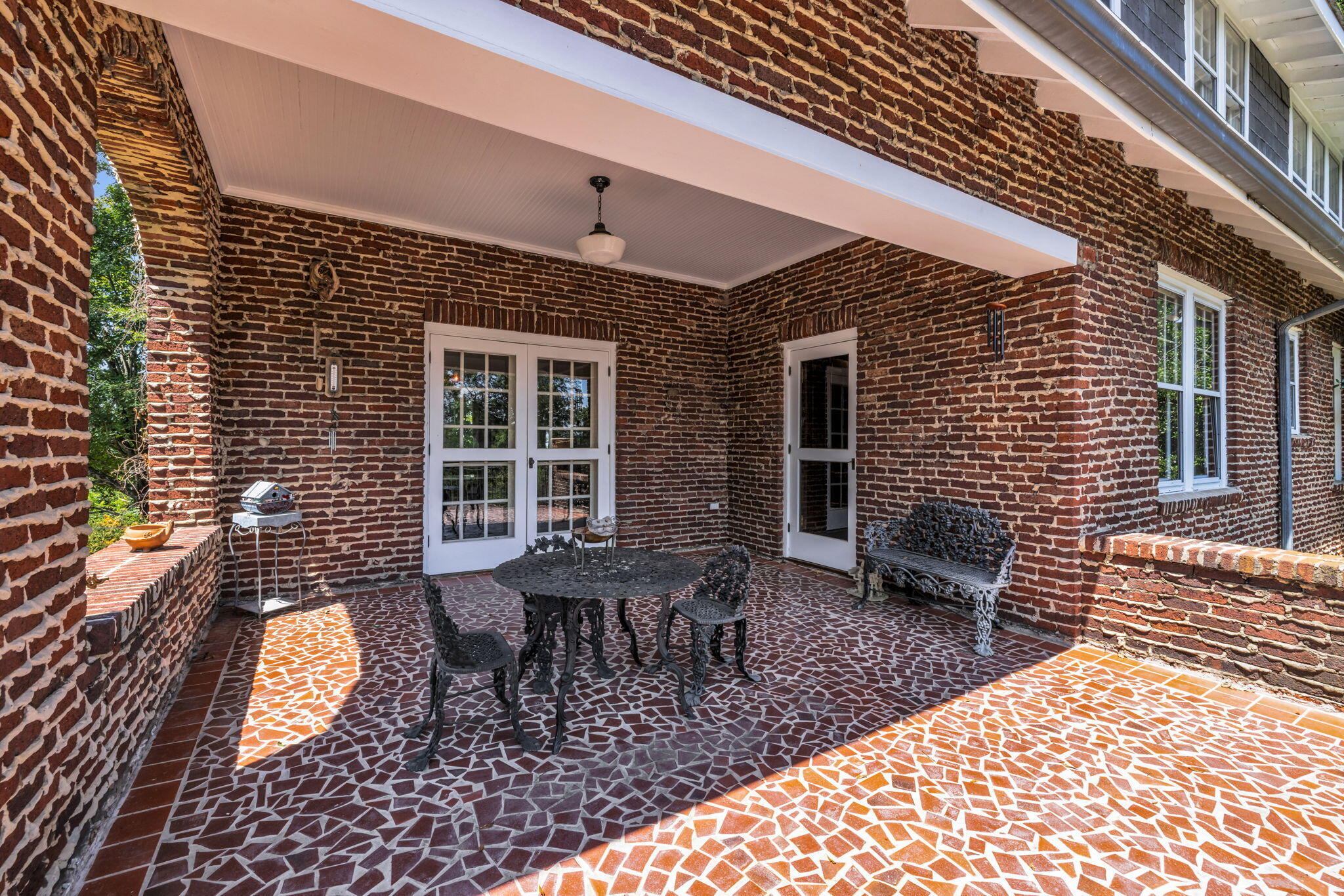 Covered brick patio with patterned tile flooring and ornate black metal dining furniture.