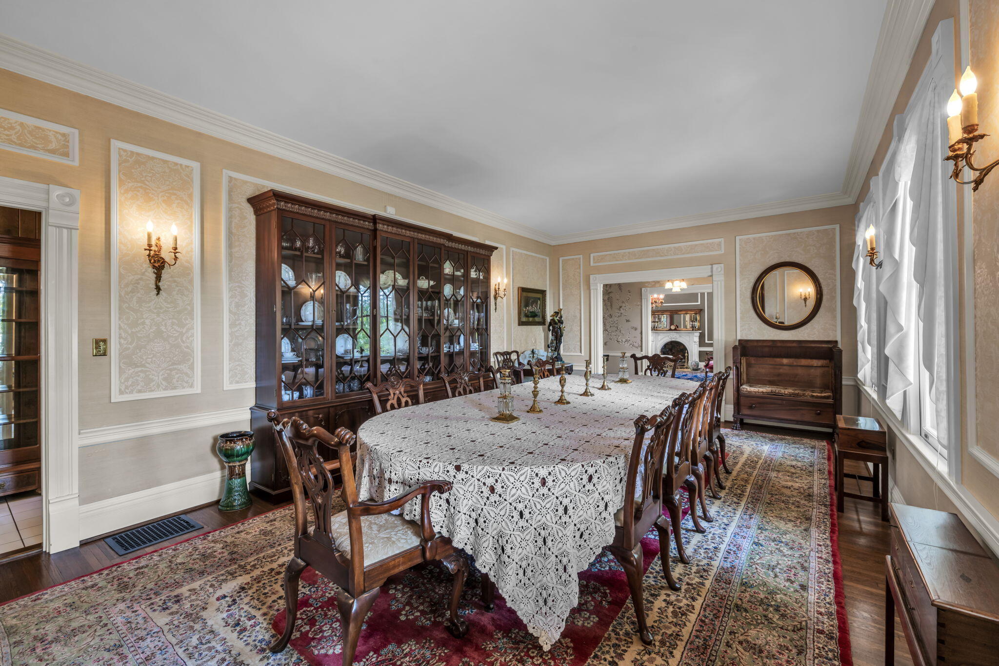 Formal dining room with a lace-covered table, carved chairs, and a large glass-front china cabinet.