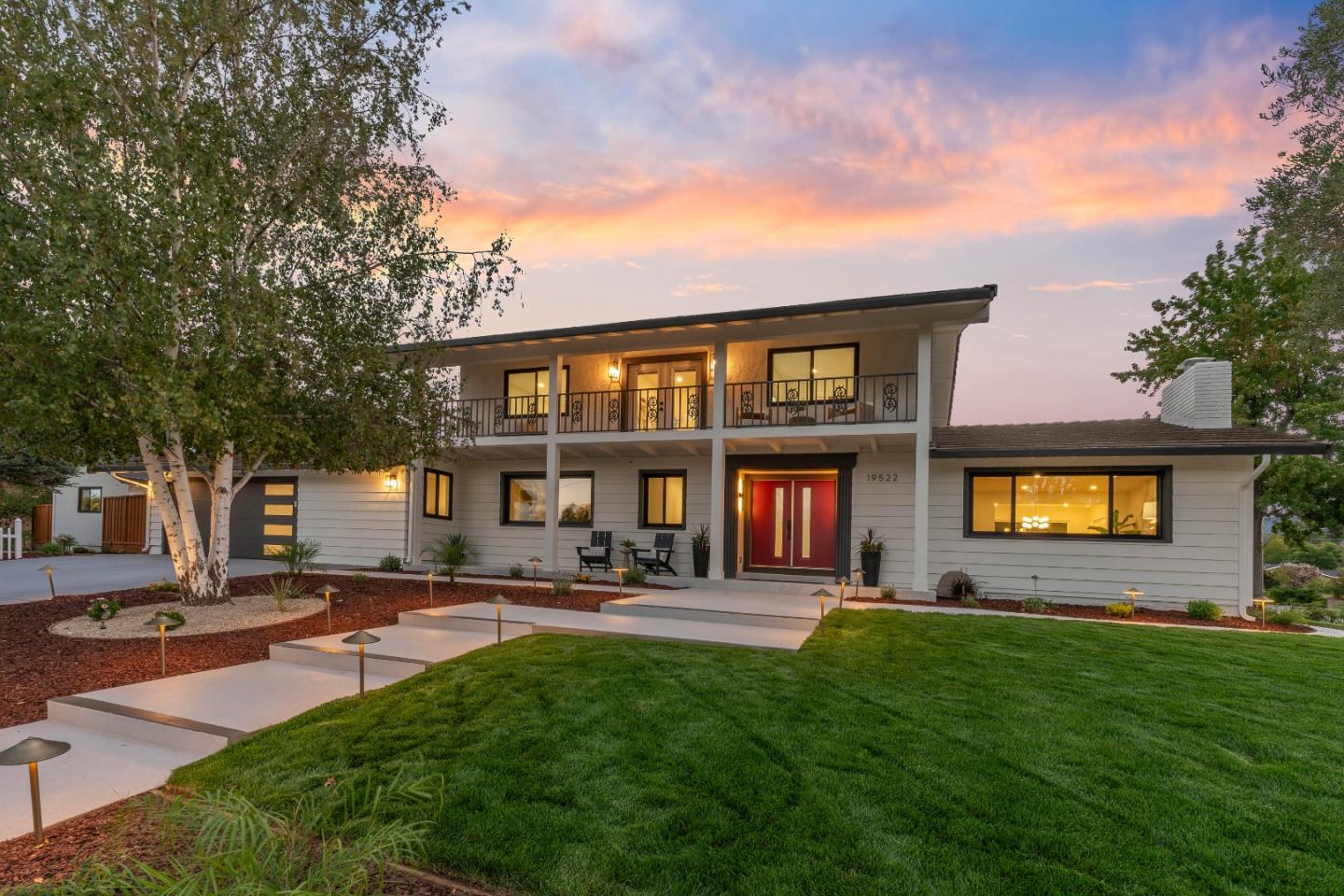 Modern two-story home with a long balcony and red double doors at dusk.