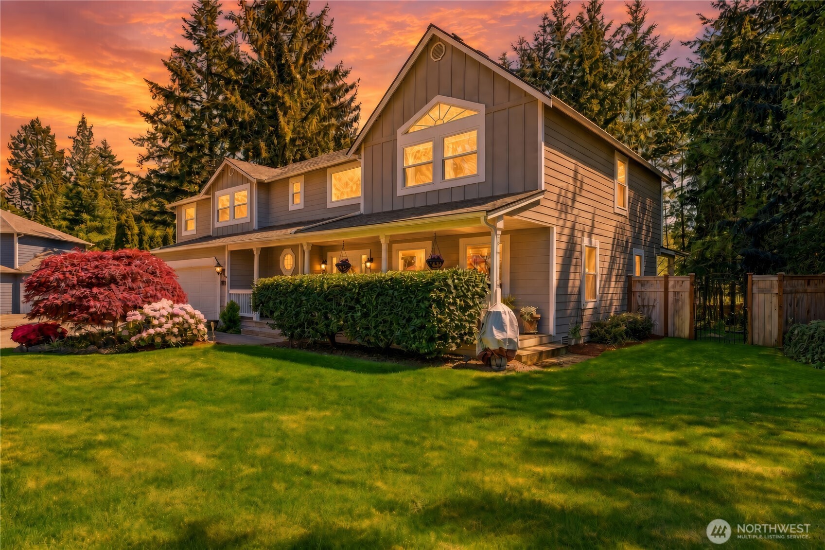 Two-story gray home with a covered porch and landscaped lawn beneath a colorful sunset sky.