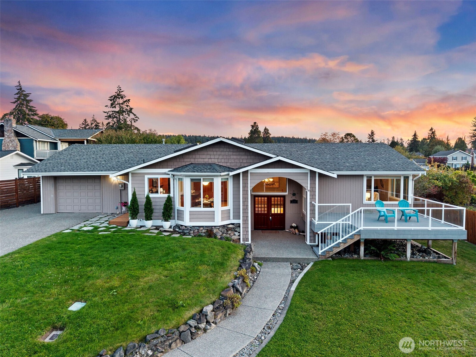 Single-story home with attached garage and raised deck beneath a colorful sunset sky.