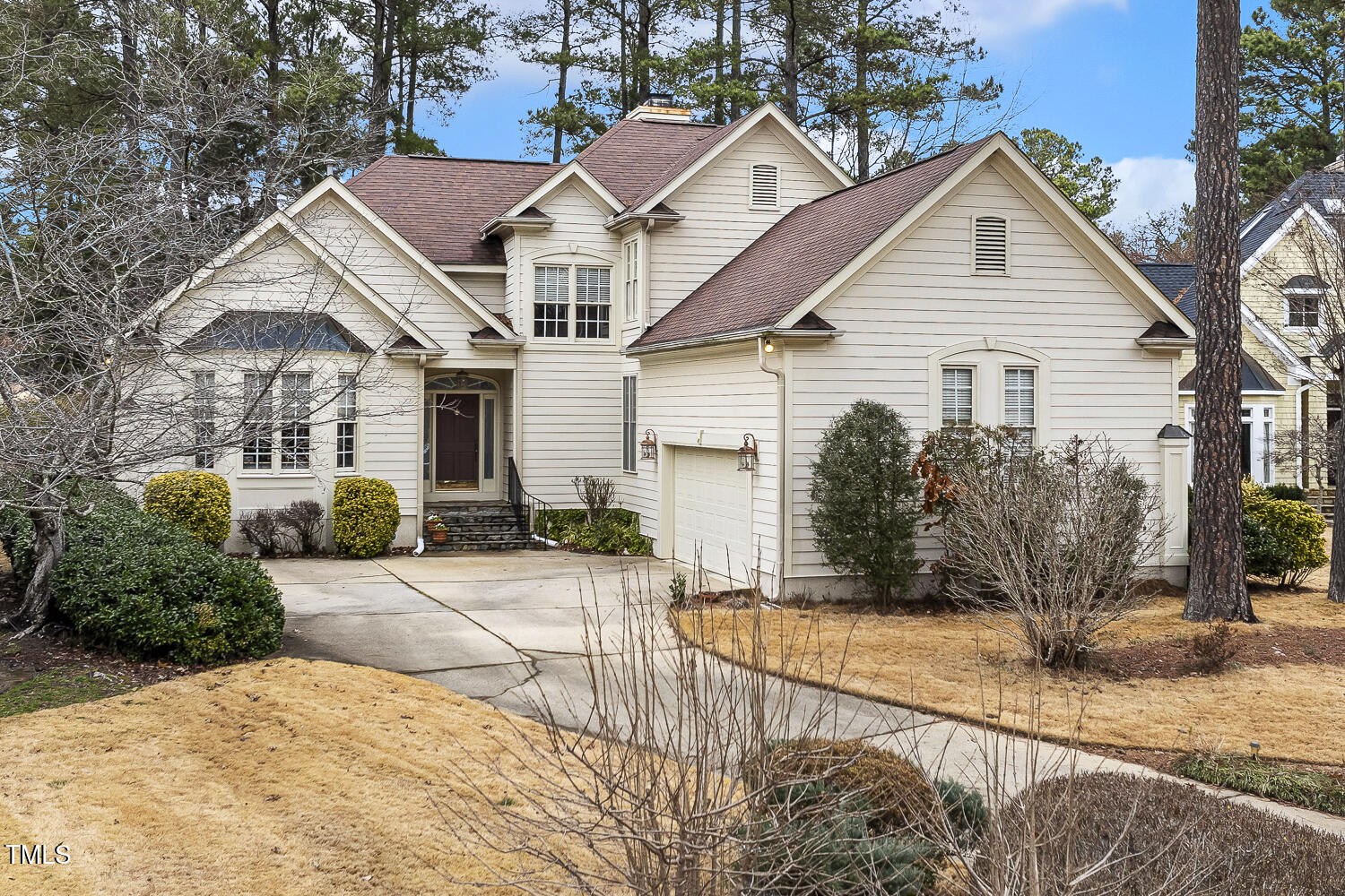 Cream-sided home with multiple gables, reddish-brown roofs, an attached garage, and a curving driveway.