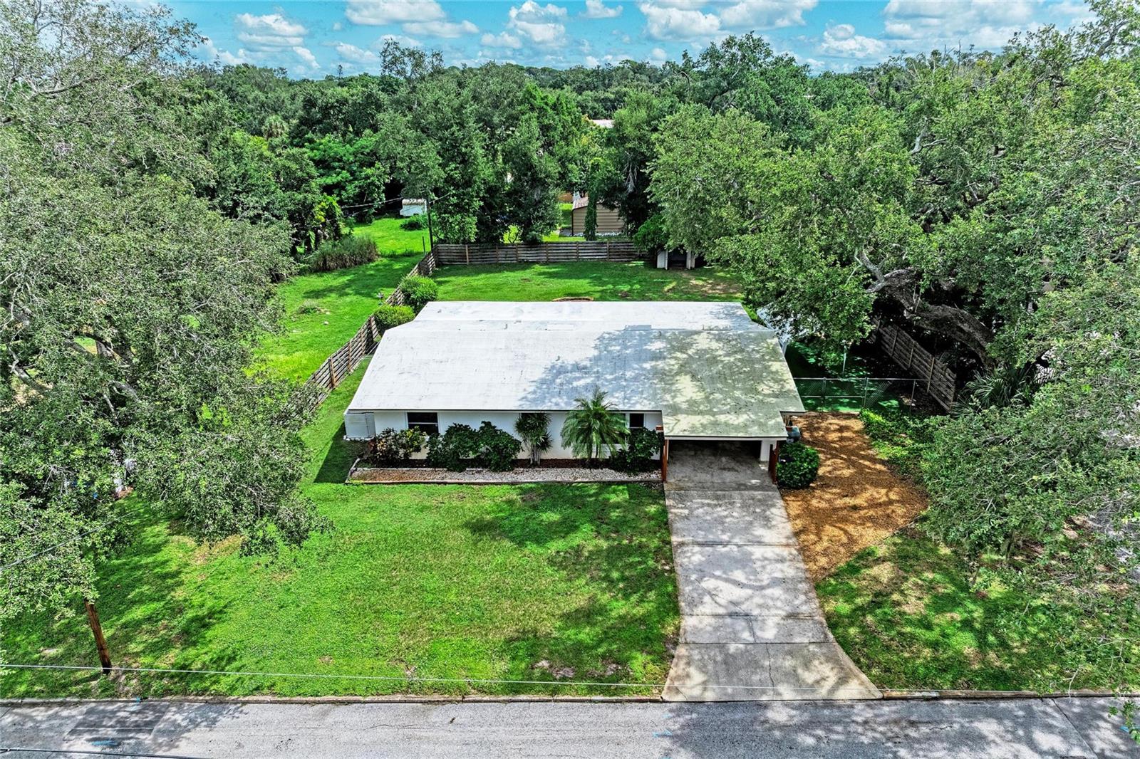 Aerial view of a single-story home with a broad lawn, mature trees, and a long driveway.