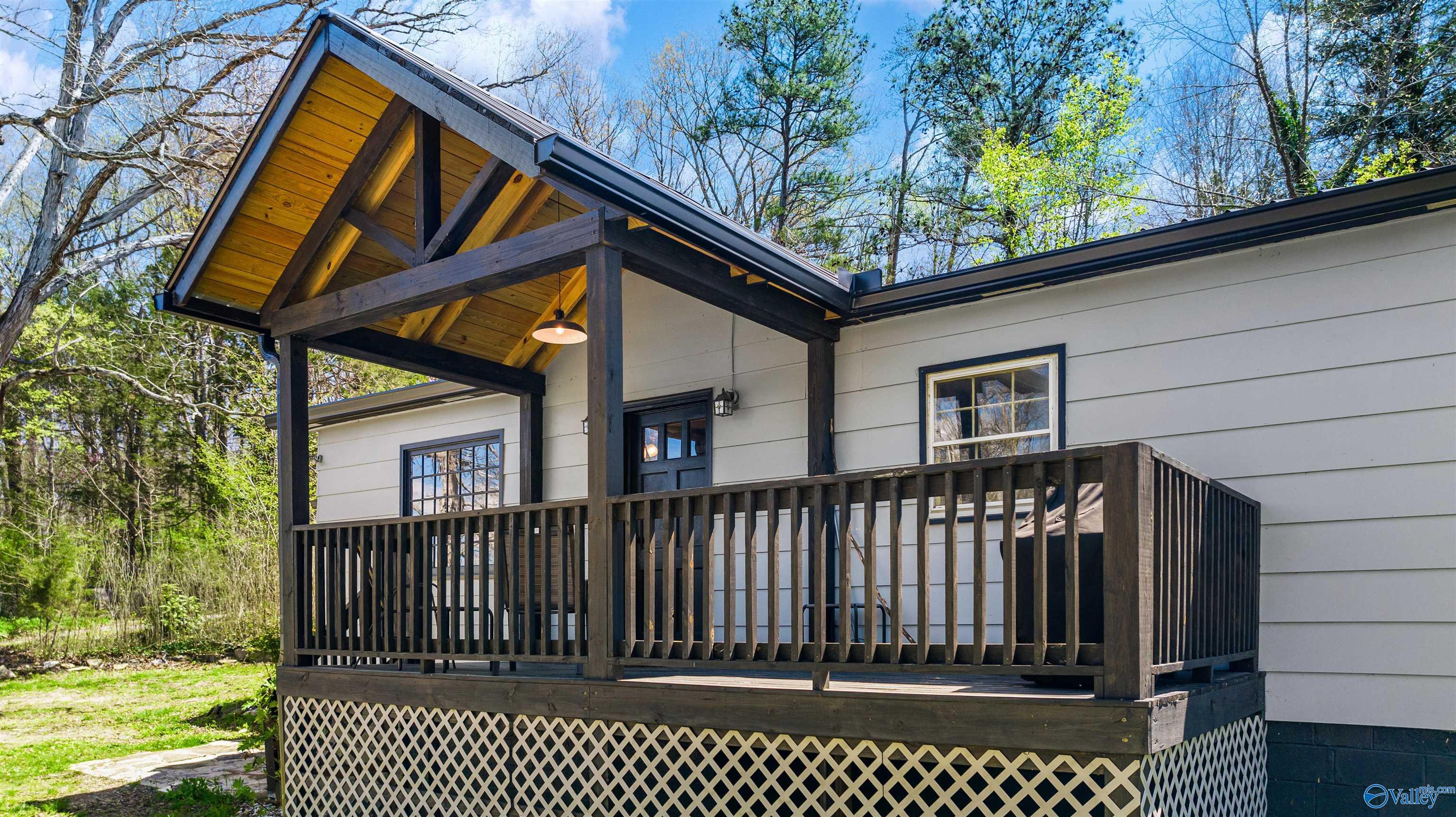 Home exterior with a dark timber-framed porch, wood ceiling, and raised deck among trees.