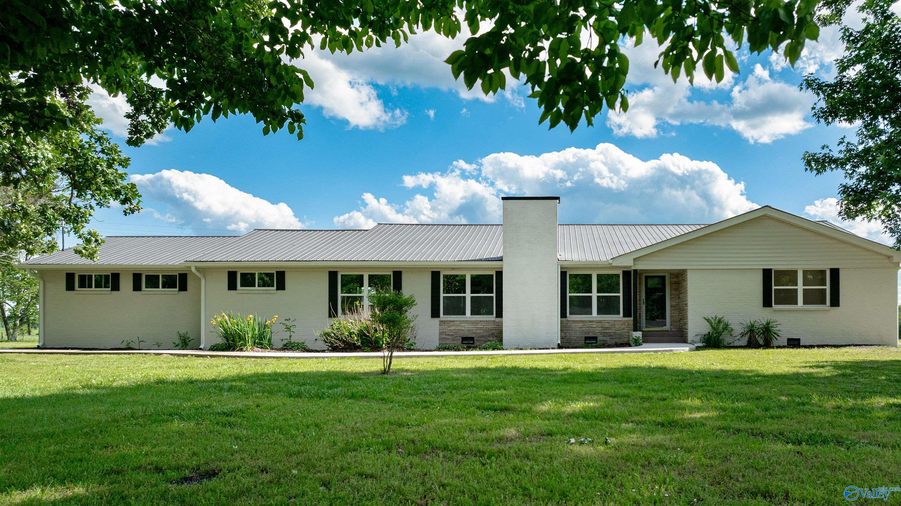 Single-story ranch house with a metal roof, central chimney, and broad green lawn.