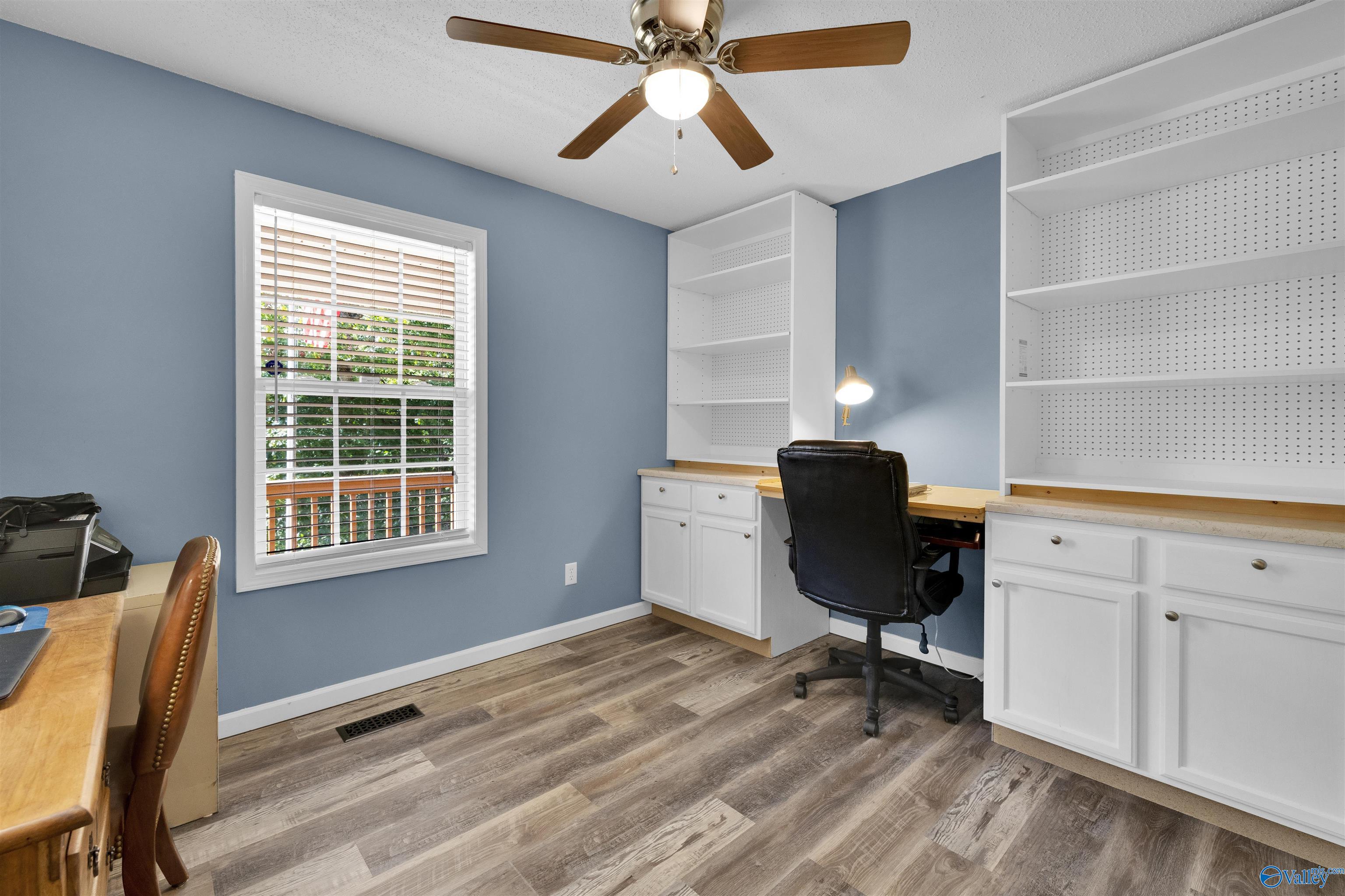 Home office with built-in white shelving and desk, blue walls, and a window with blinds.