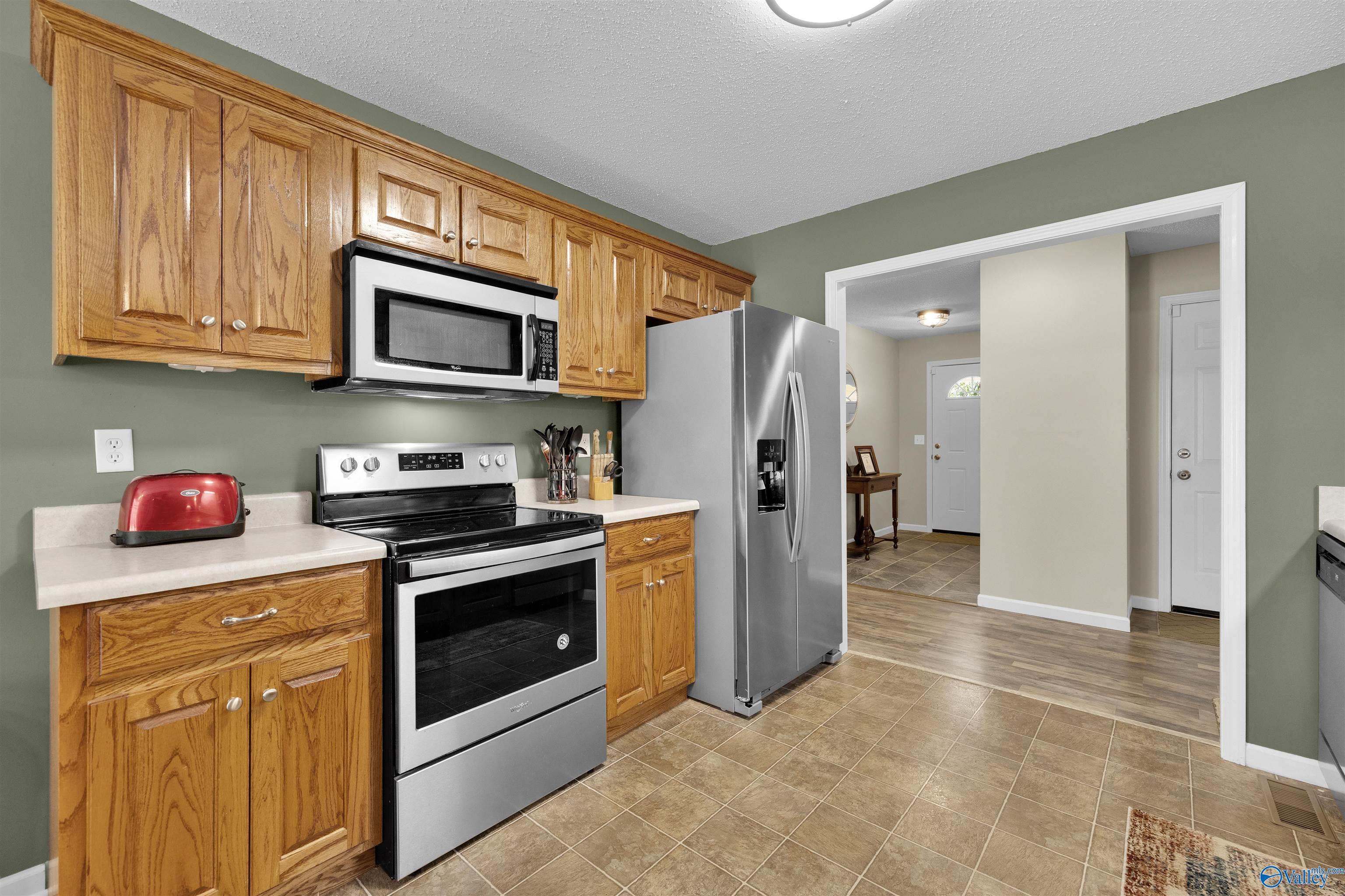 Kitchen with oak cabinets, stainless steel appliances, and tan tile flooring.