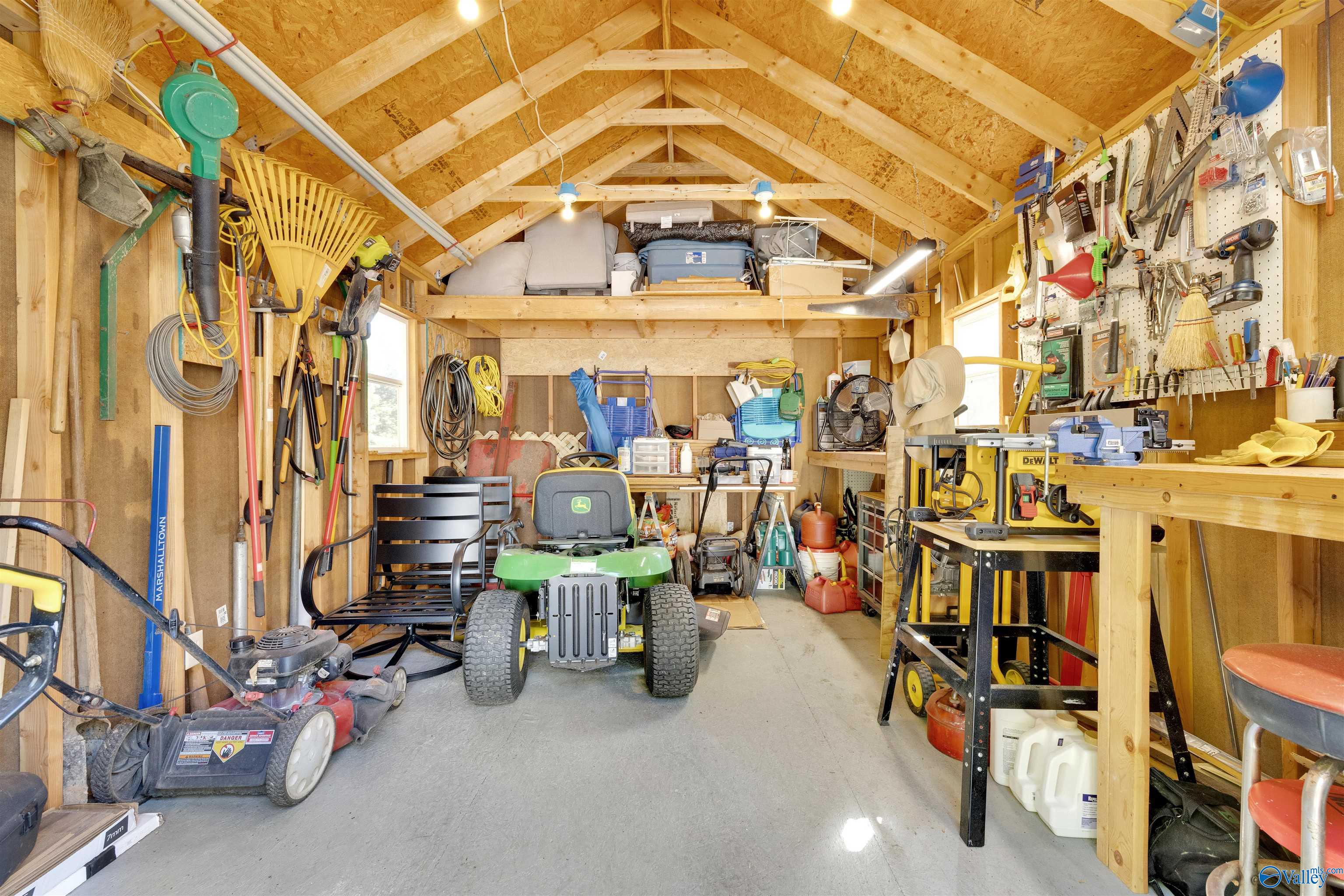 Wooden garage workshop filled with tools, workbenches, and a green riding mower.