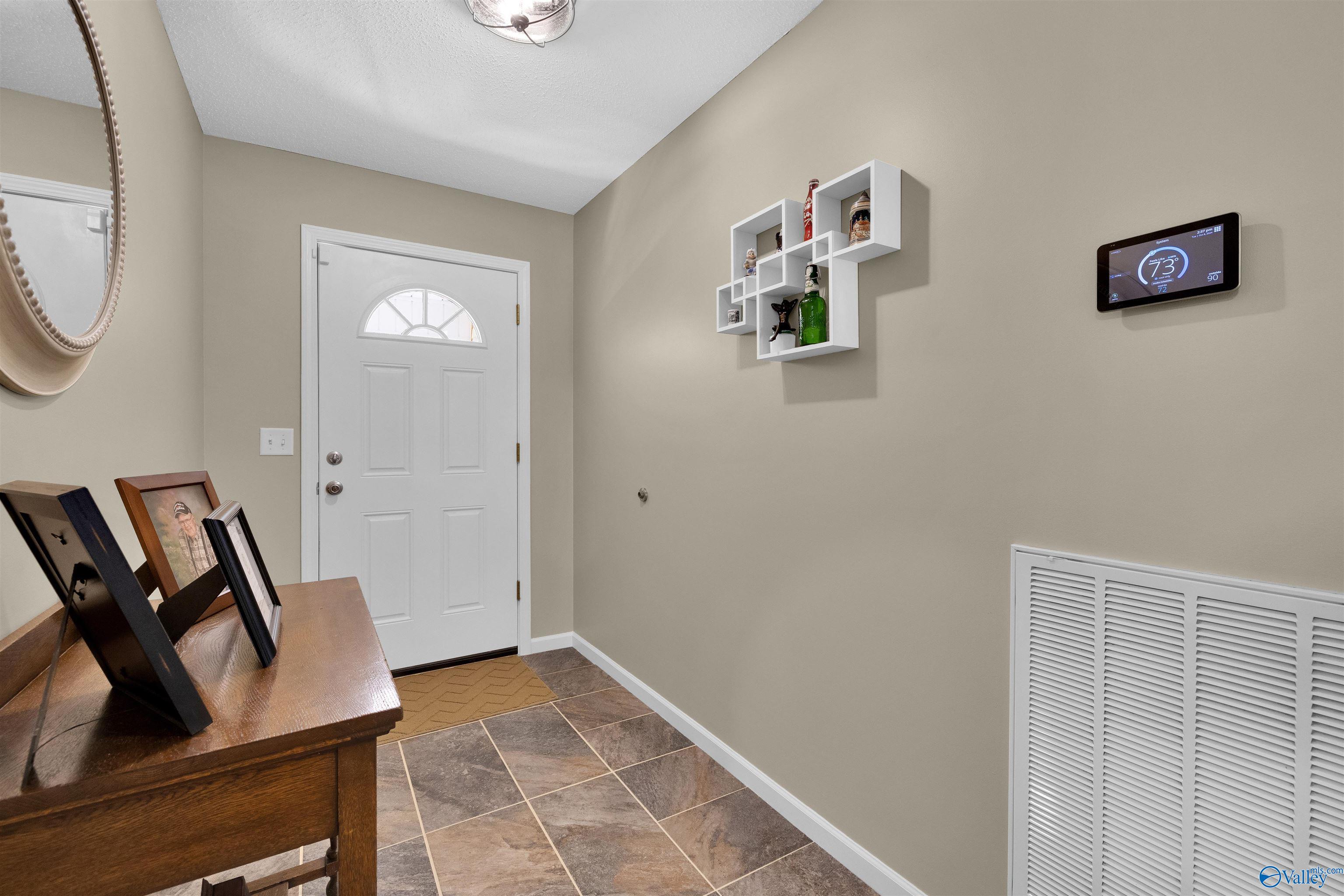 Entry foyer with a white half-circle-window door, brown tile flooring, and a wooden console table.