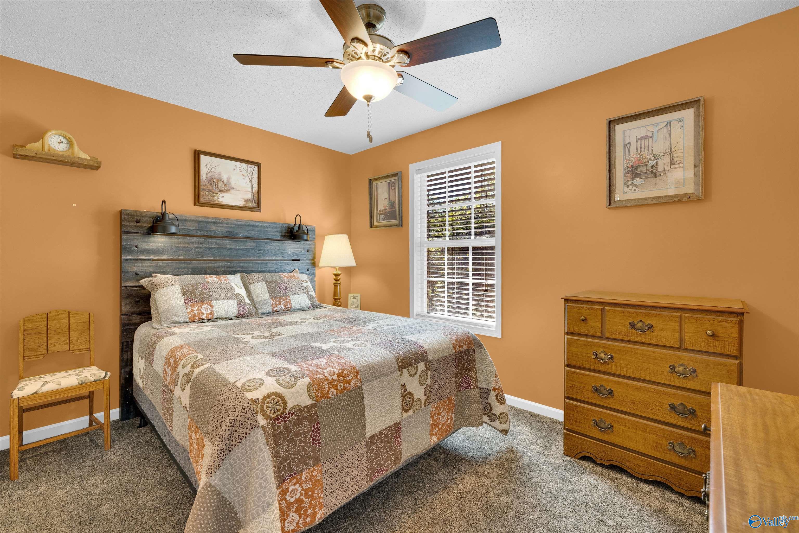 Bedroom with ochre walls, patchwork quilt, rustic wood headboard, and wooden dresser.