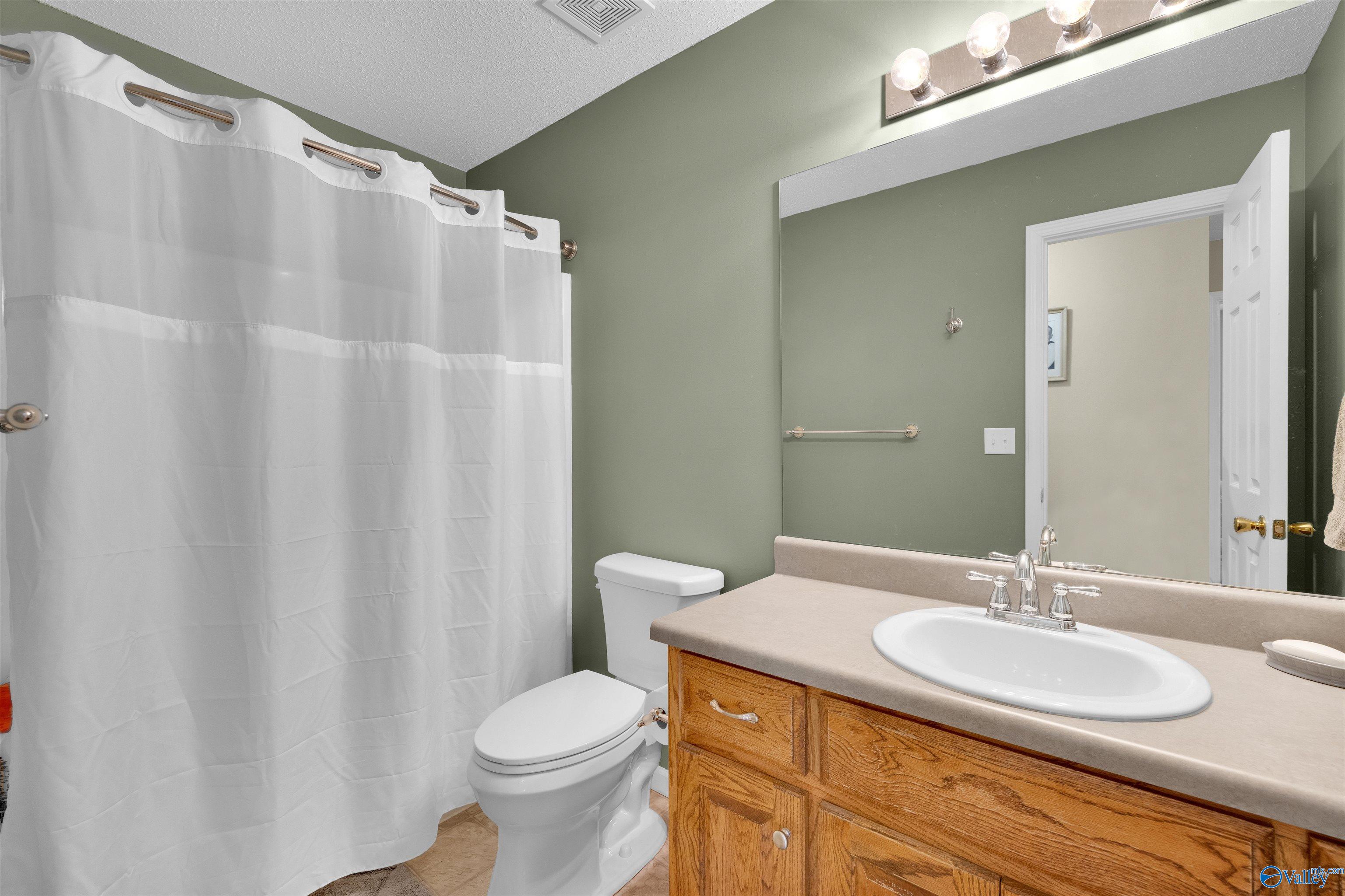 Bathroom with sage-green walls, a white shower curtain, and a wood vanity with an oval sink.