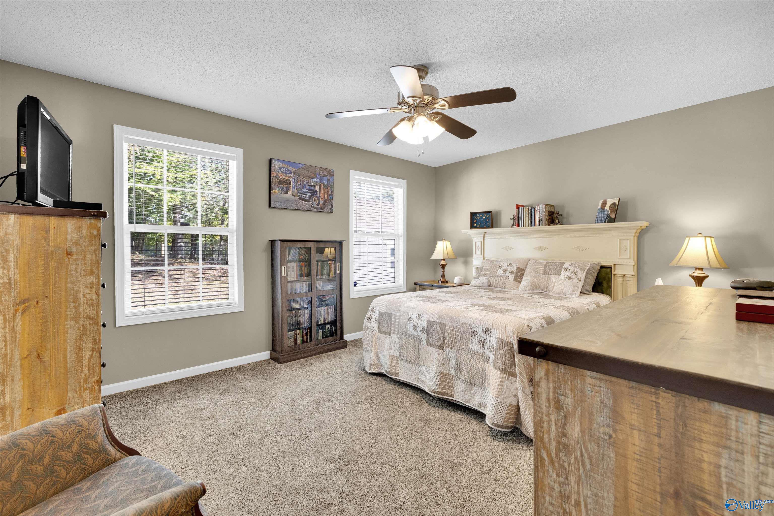 Furnished bedroom with a large bed, two bright windows, ceiling fan, and rustic wood furniture.