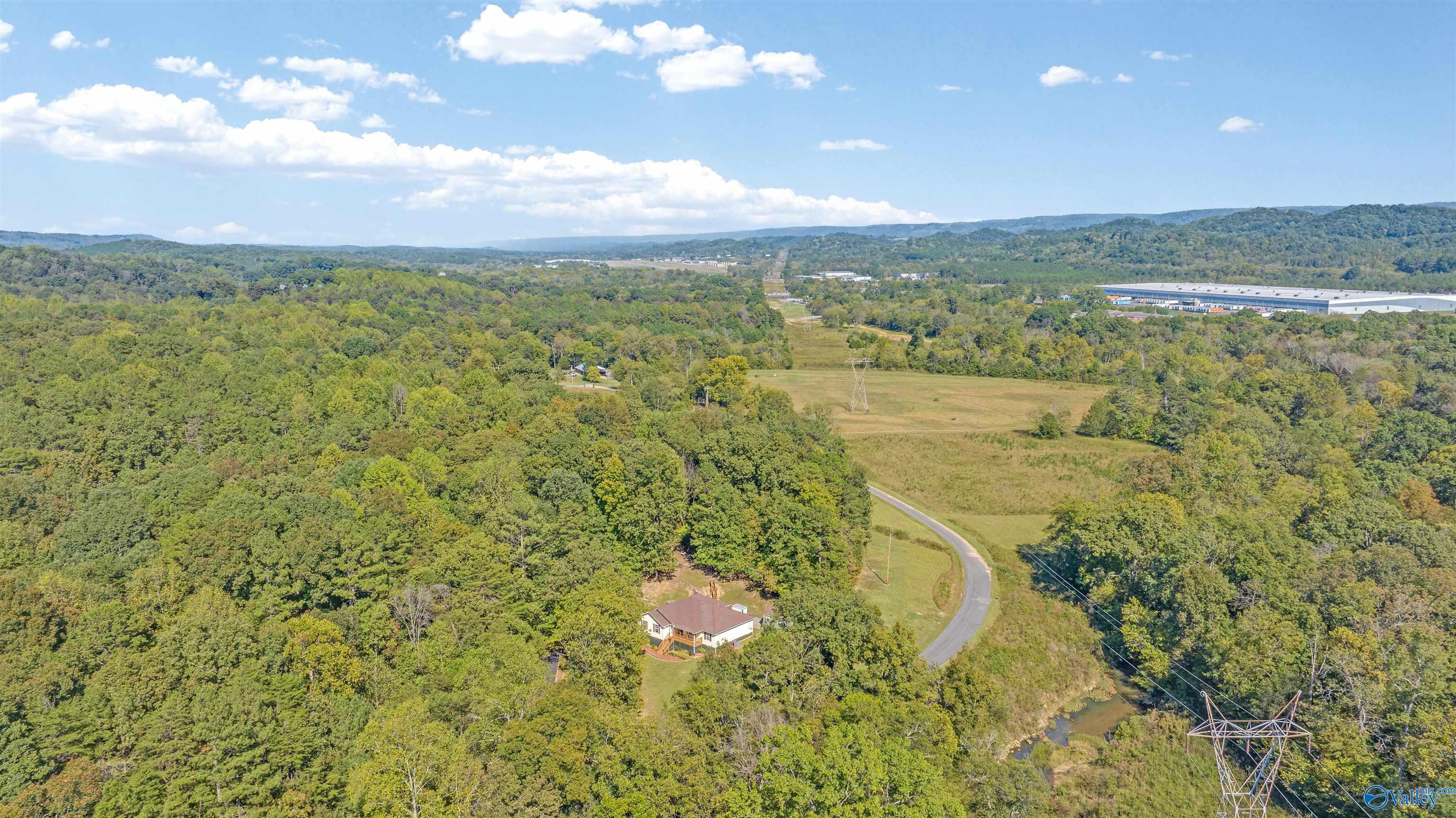 Aerial view of a house amid wooded acreage, open fields, and a winding road.
