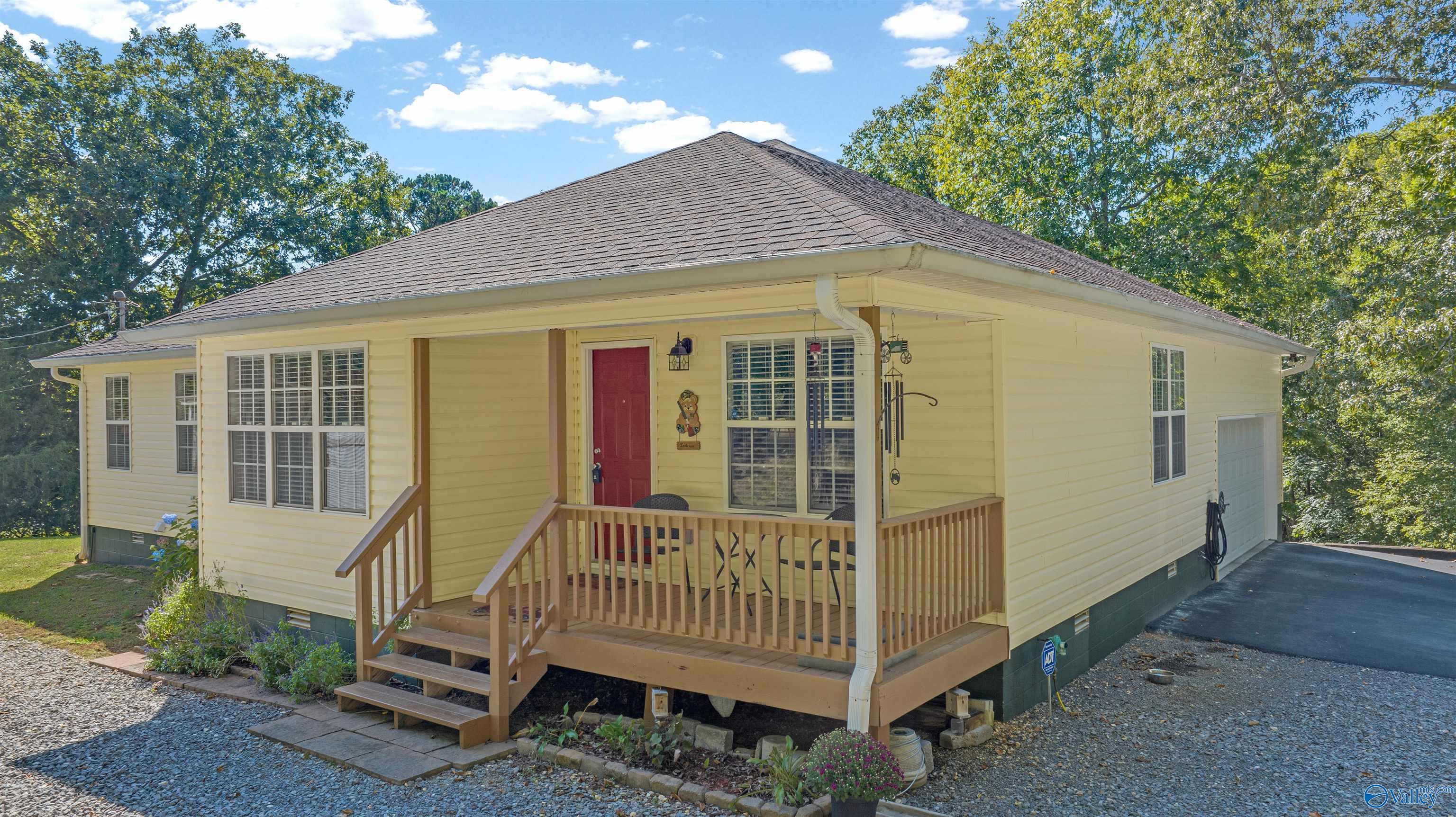 Pale yellow home with a red front door, raised wooden porch, and attached garage.