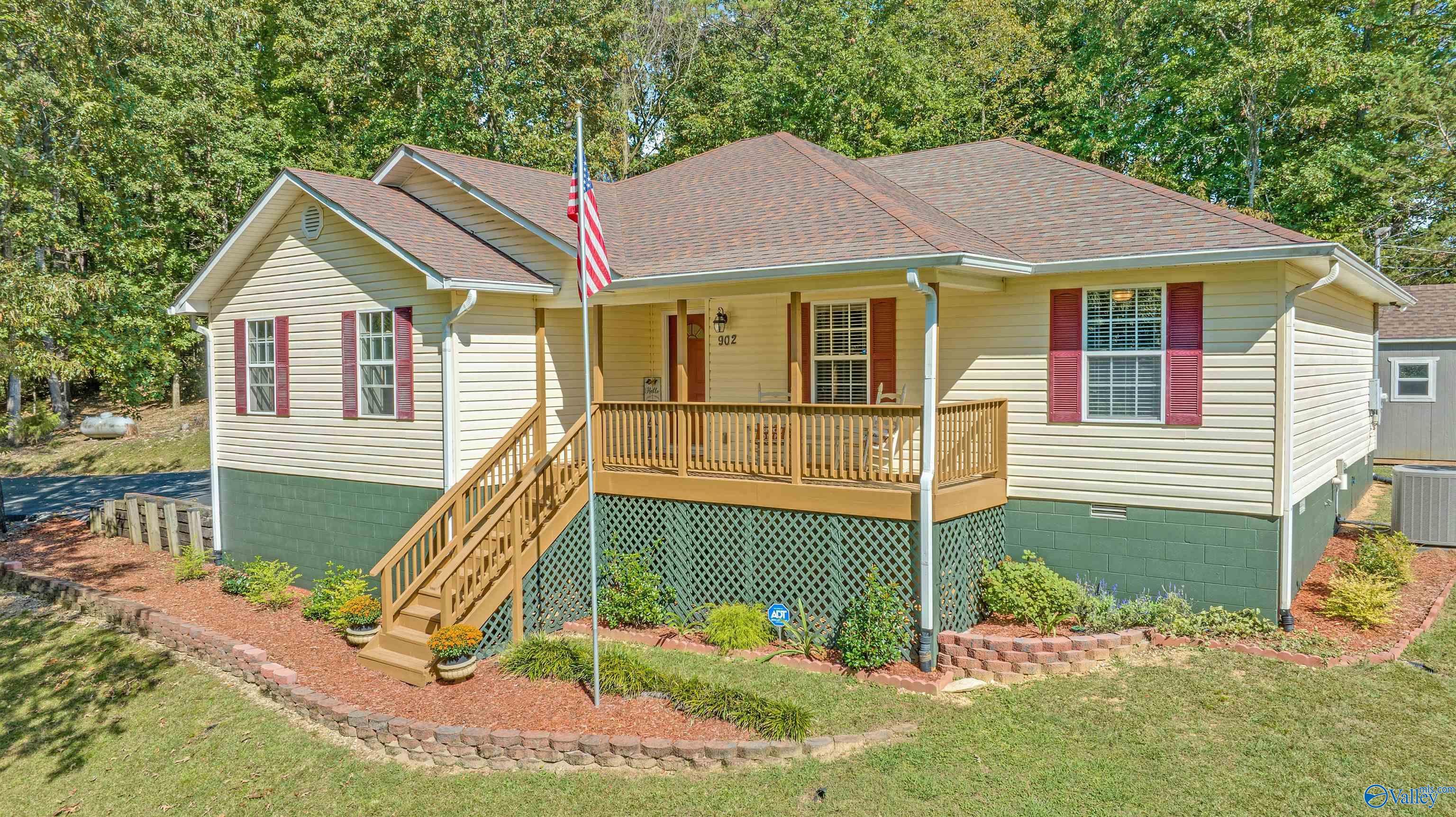 Single-story home with raised wooden front porch, red shutters, and landscaped yard.