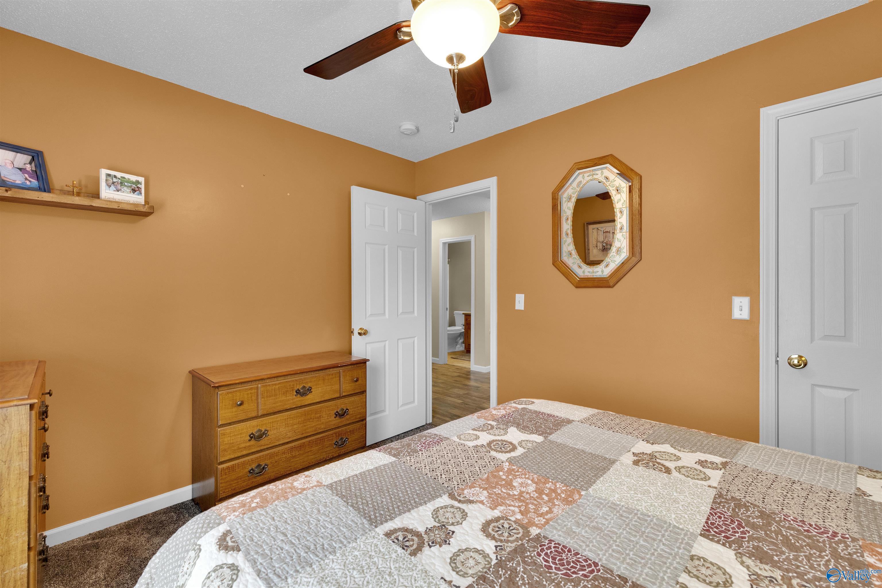 Furnished bedroom with ochre walls, a patchwork quilt, wooden dresser, and ceiling fan.