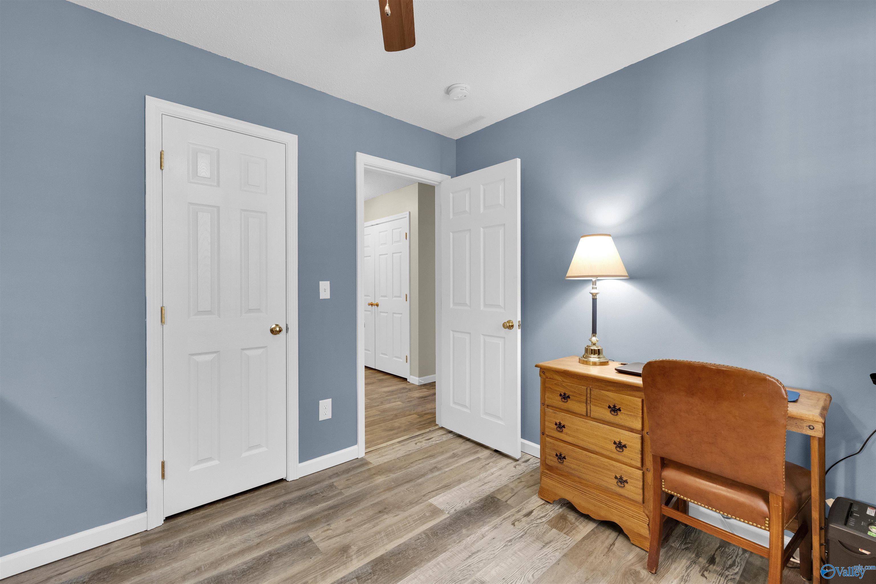 Furnished home office with blue walls, wood-look flooring, and a wooden desk and leather chair.