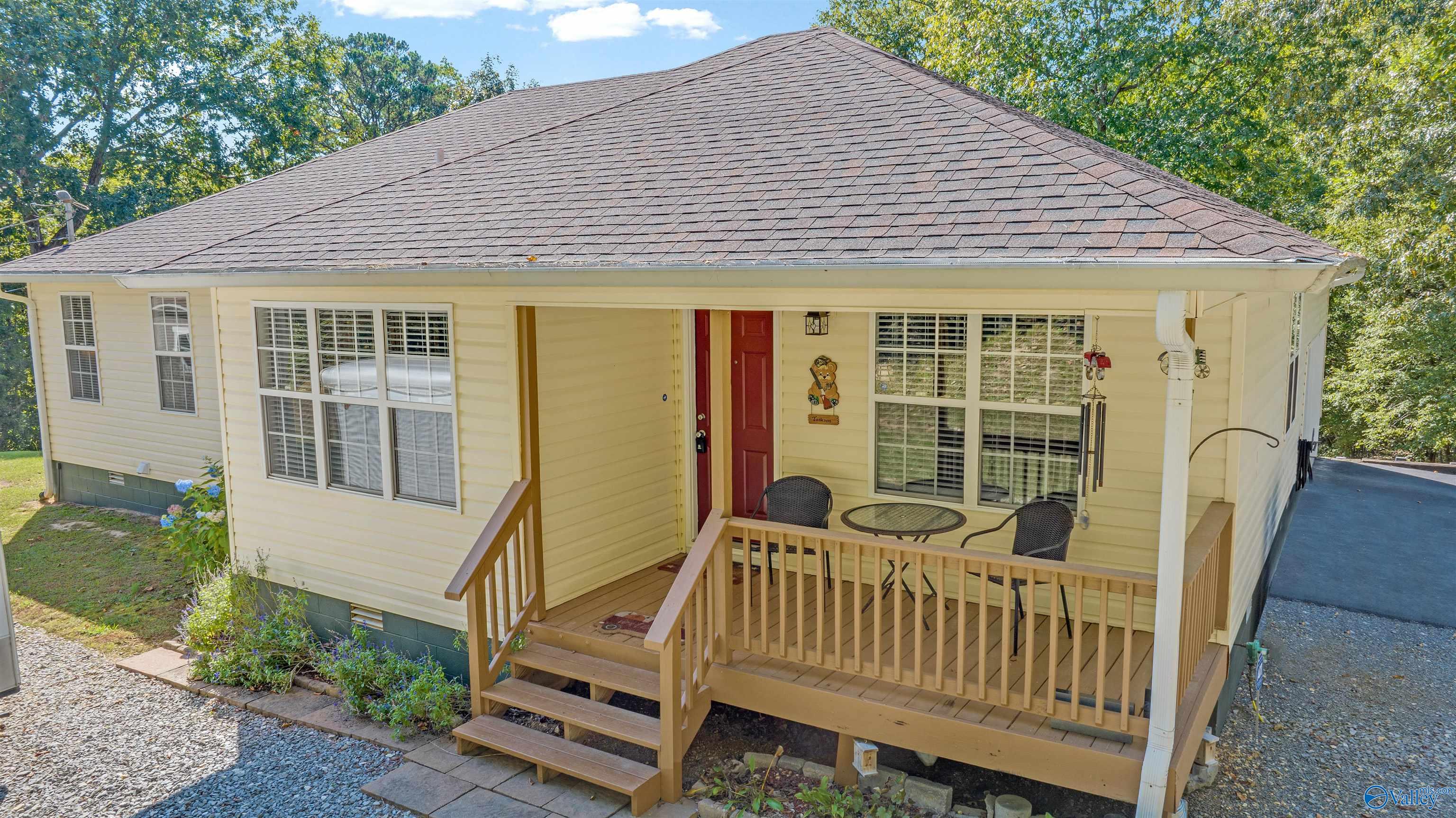 Pale yellow house with a covered, furnished front porch, red door, and steps.