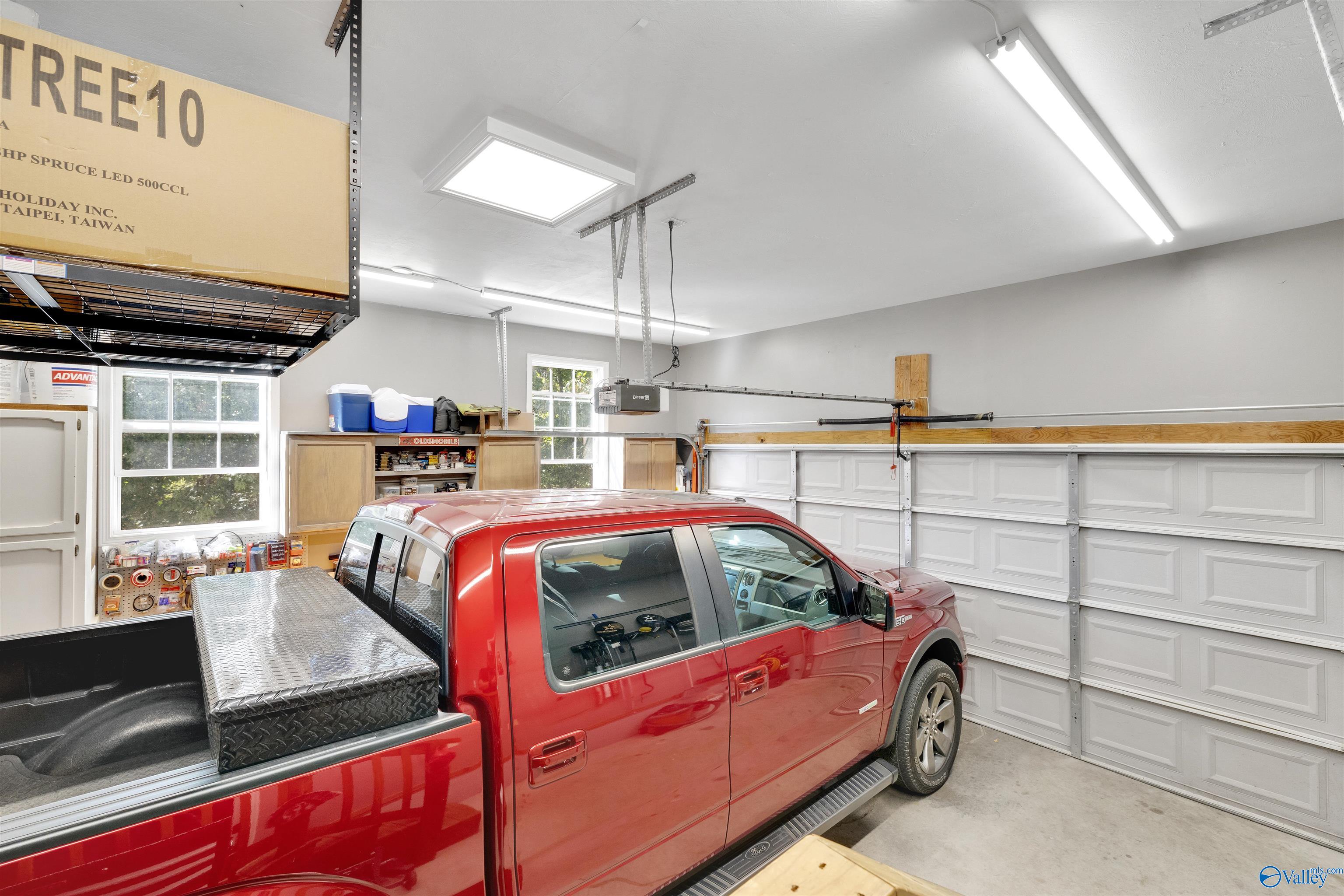 Garage with a red pickup, overhead storage rack, cabinets, and a paneled garage door.