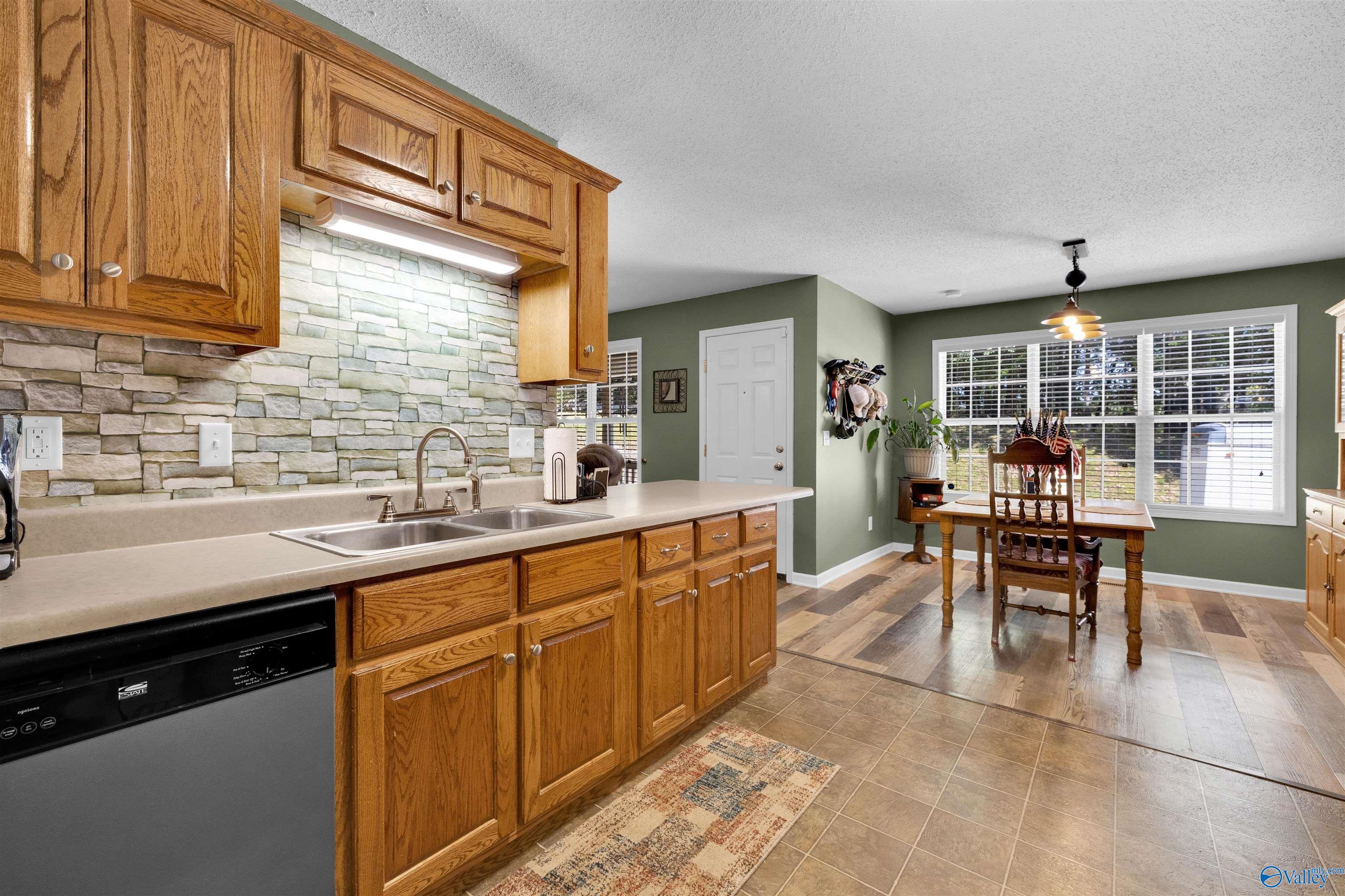 Kitchen and dining area with oak cabinets, stone backsplash, and a wooden table by large windows.